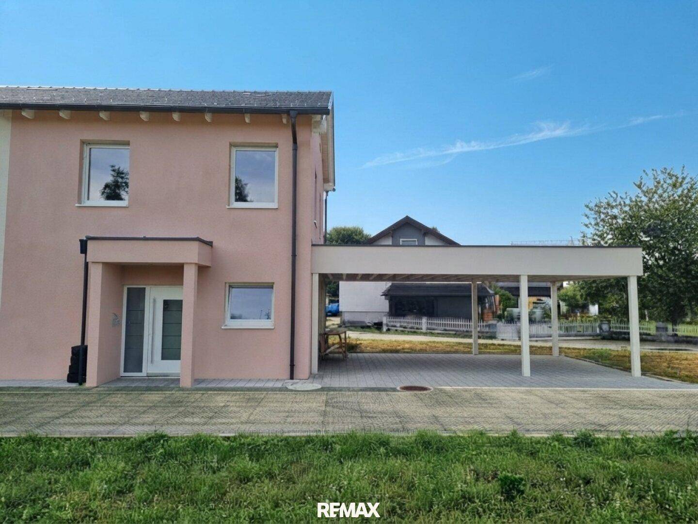 Ansicht des modernen Einfamilienhauses mit Eingangsbereich und Carport an einem sonnigen Tag.