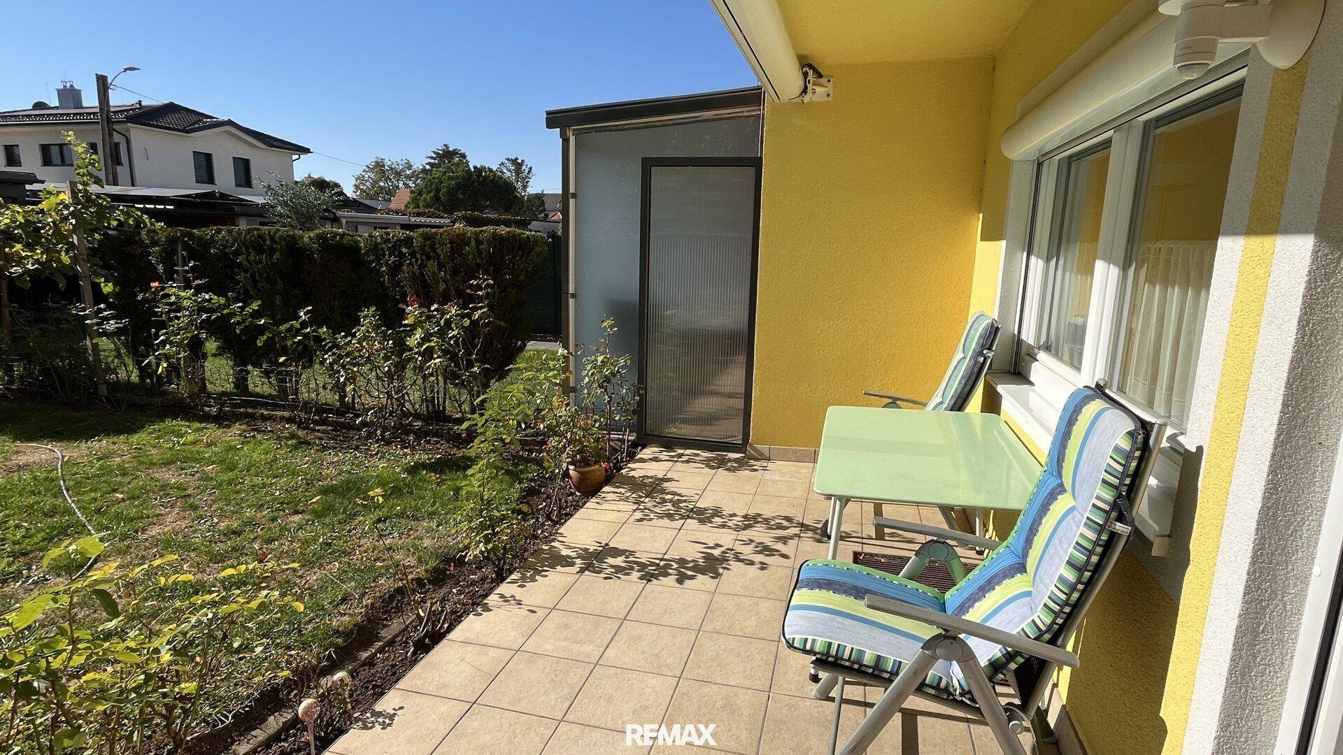 Sonniger Terrassenbereich mit Fliesenboden und Gartenmöbeln, umgeben von Grün.
