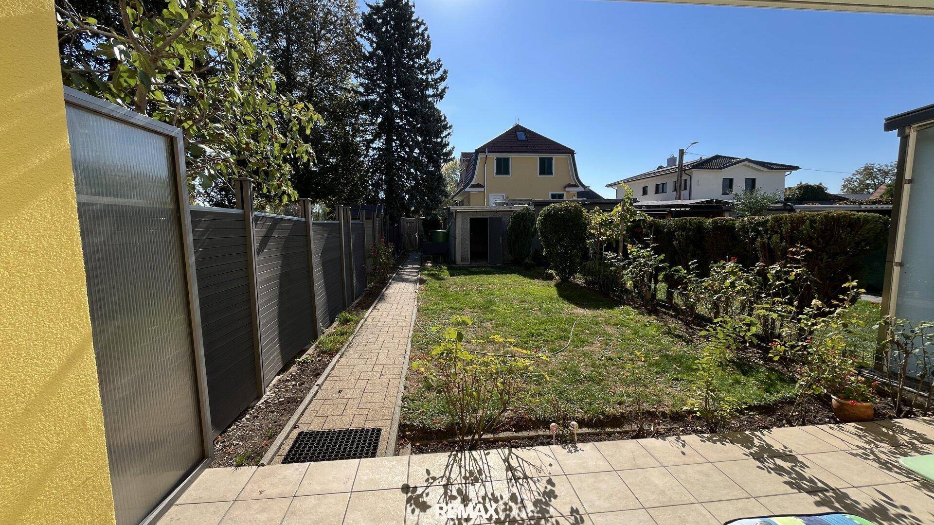 Langer, schmaler Garten mit Rasenfläche, gepflastertem Weg und Gartenhaus.