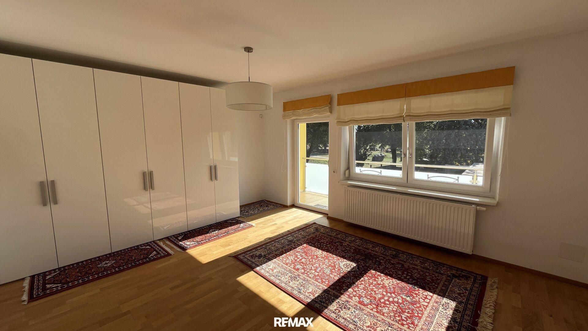 Helles Schlafzimmer mit Parkettboden, großem Kleiderschrank und Balkonzugang.