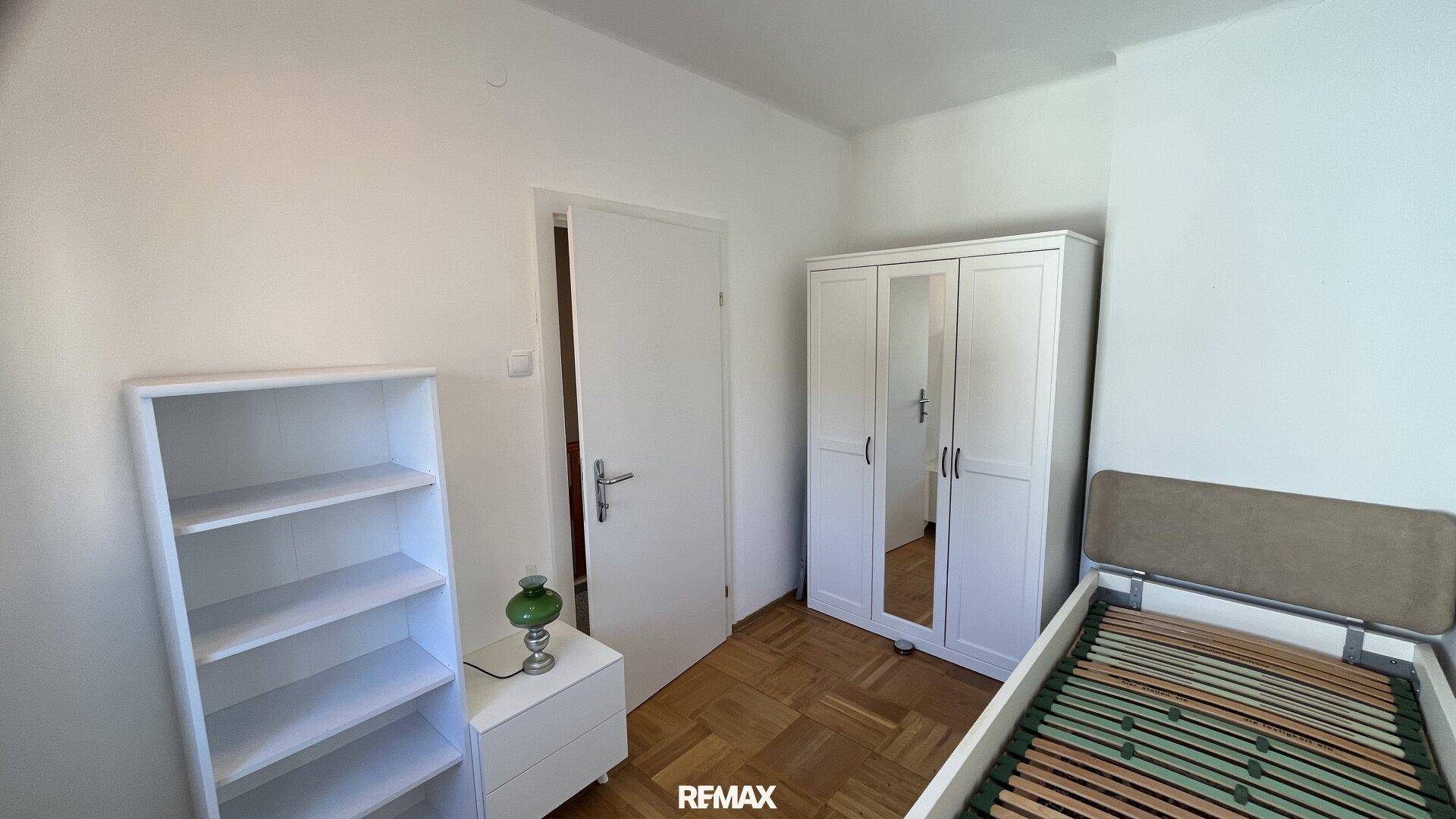 Helles Schlafzimmer mit Parkettboden, Kleiderschrank und Regal.