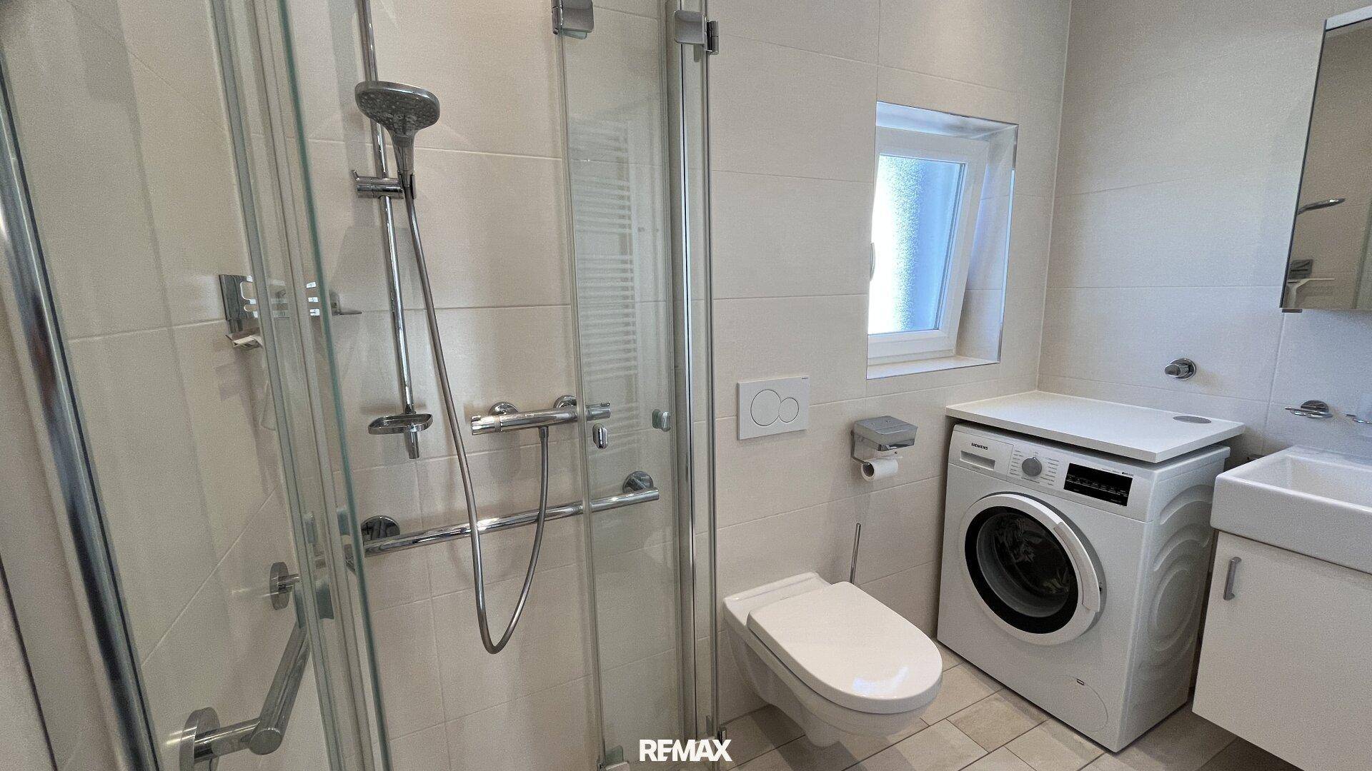 Modernes Badezimmer mit Dusche, WC, Waschmaschine und Fenster.
