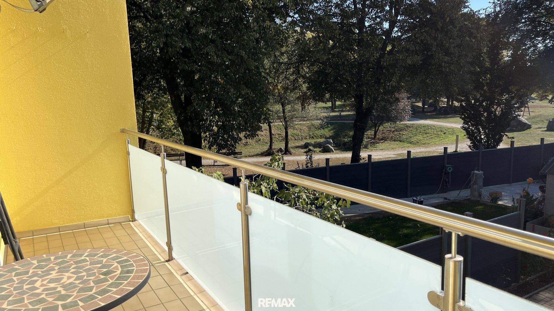 Balkon mit Glasgeländer und weitem Blick auf eine grüne Parklandschaft.