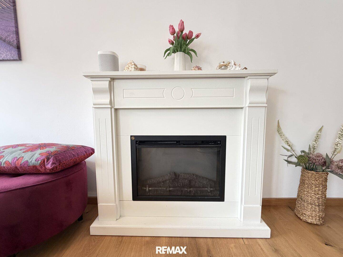 Dekorativer Kamin mit weißem Mantel und Blumen, ein gemütlicher Blickfang im Wohnzimmer.