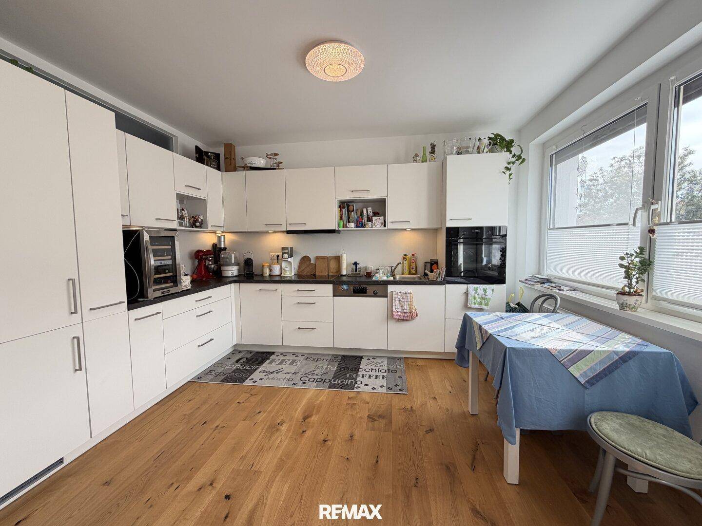 Moderne Einbauküche mit weißen Schränken, dunkler Arbeitsplatte und Essbereich am Fenster.