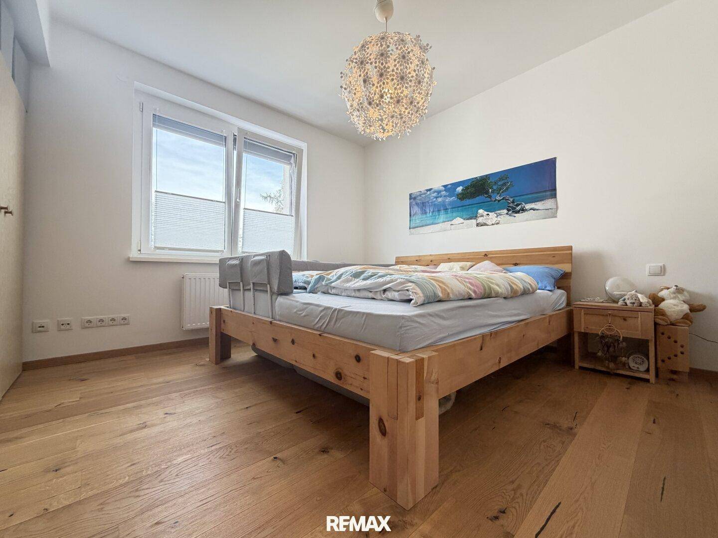 Schlafzimmer mit Holzbett, Parkettboden und großem Fenster für viel Tageslicht.
