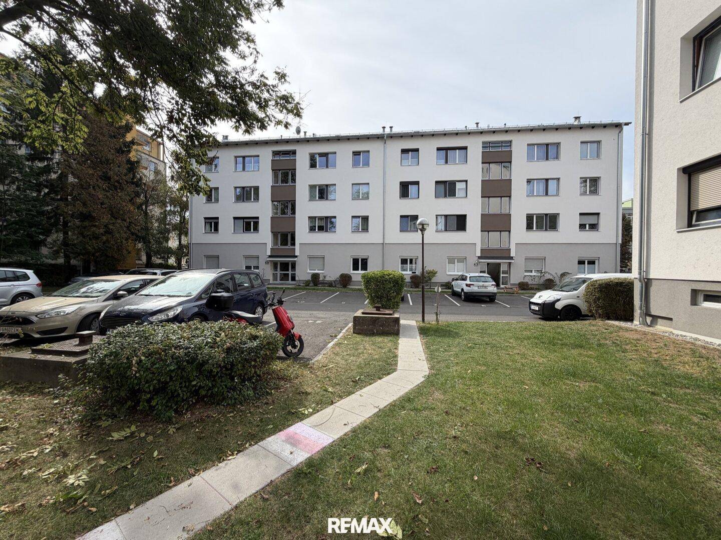 Mehrfamilienhaus mit Parkplätzen und Grünflächen in einer städtischen Umgebung.