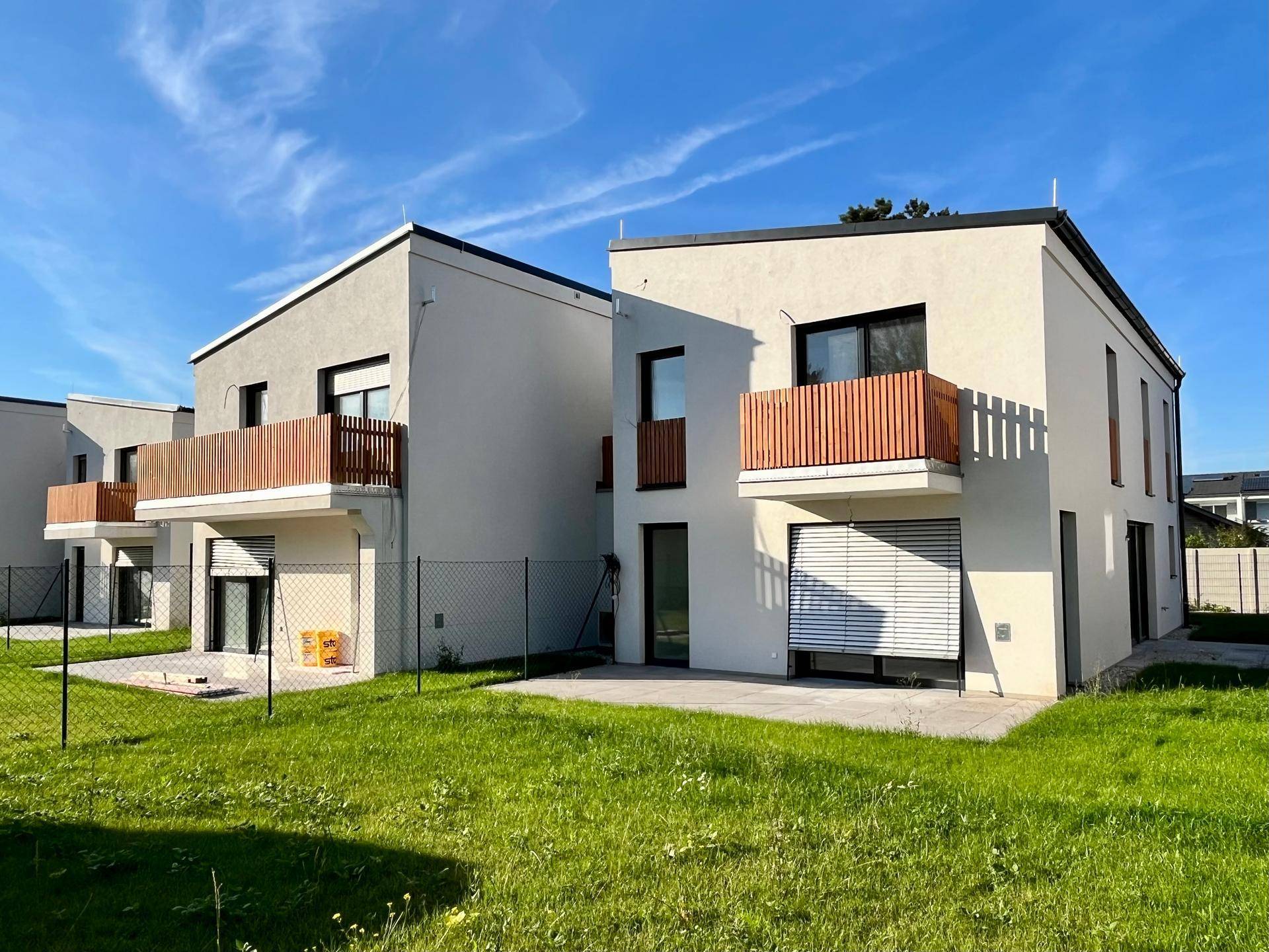 Zwei moderne Reihenhäuser von hinten mit kleinen Gärten und Balkonen im Sonnenlicht.