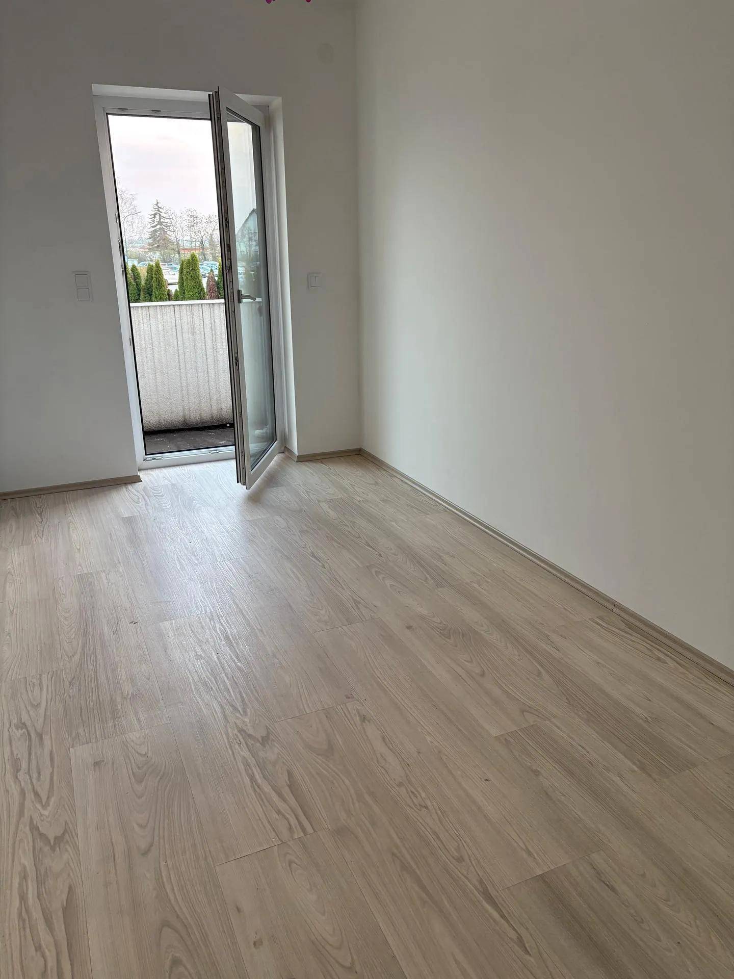 Helles Zimmer mit Laminatboden und direktem Zugang zu einem kleinen Balkon.