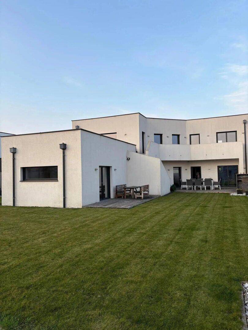 Gepflegter Gartenbereich mit großer Rasenfläche, Holzterrasse und Sitzgelegenheiten im Freien.