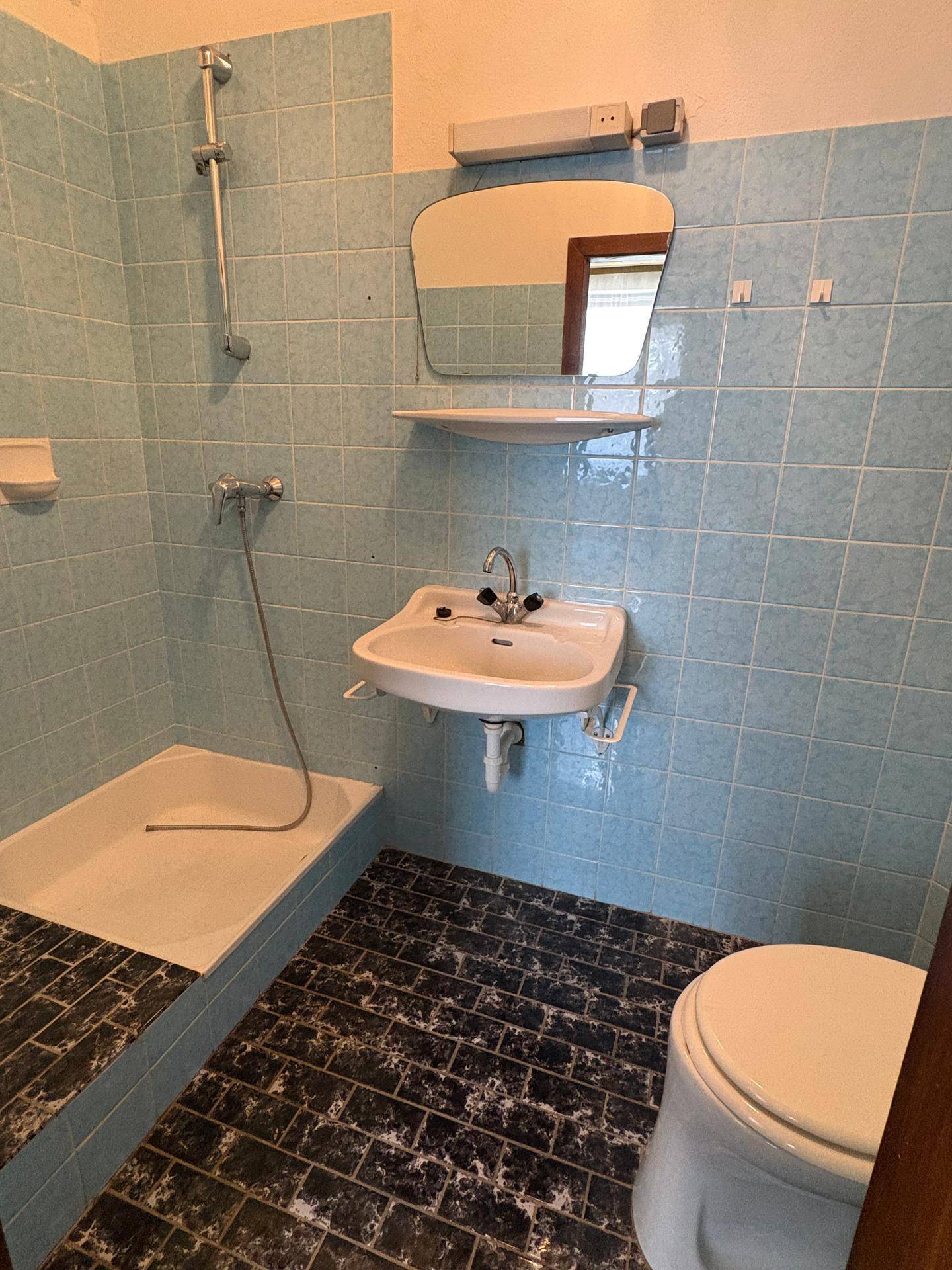 Badezimmer mit blauen Fliesen, Dusche, WC und Waschbecken in einfachem Stil.