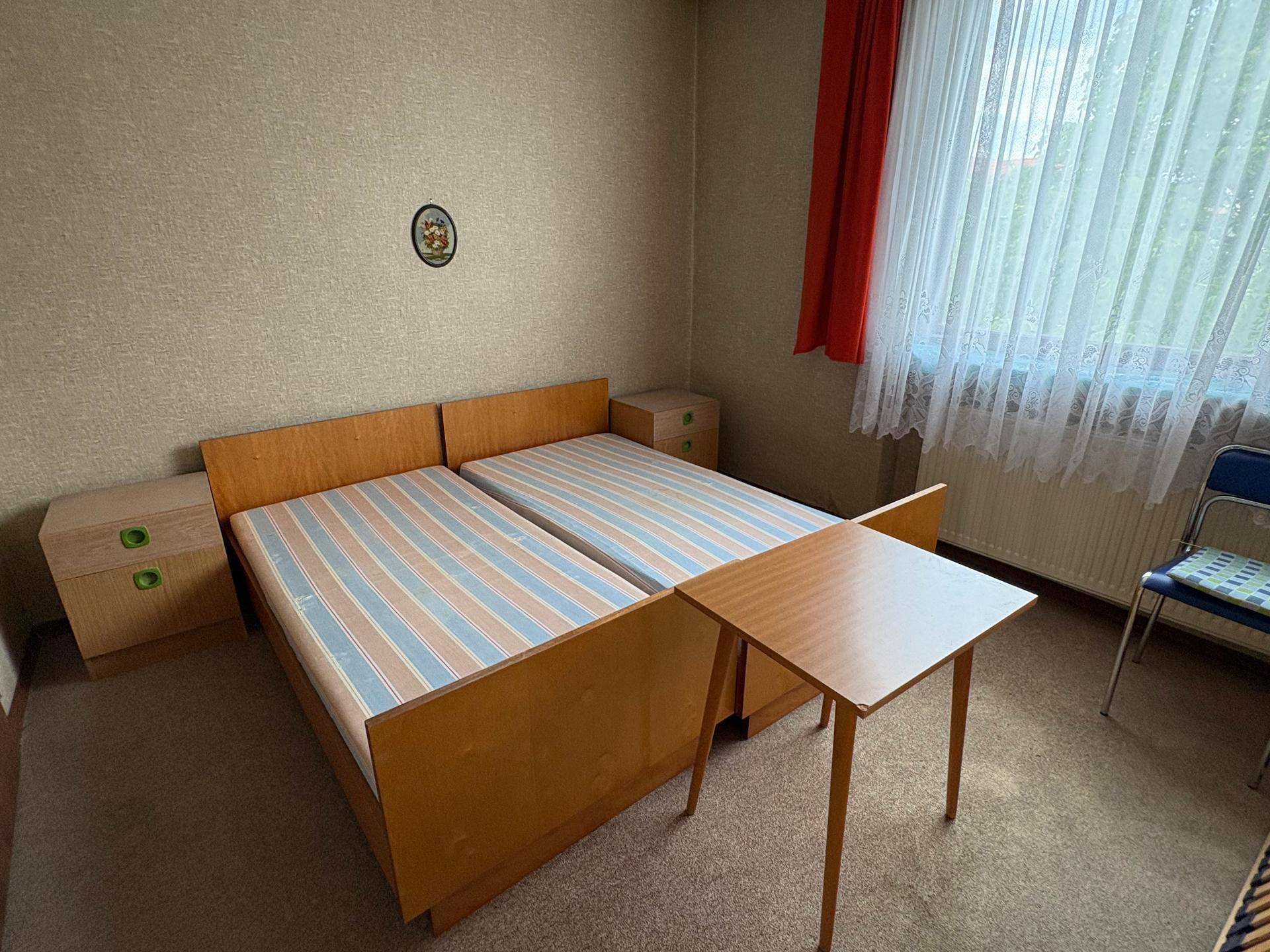 Schlafzimmer mit zwei Einzelbetten, Teppichboden und Fenster mit Vorhängen.