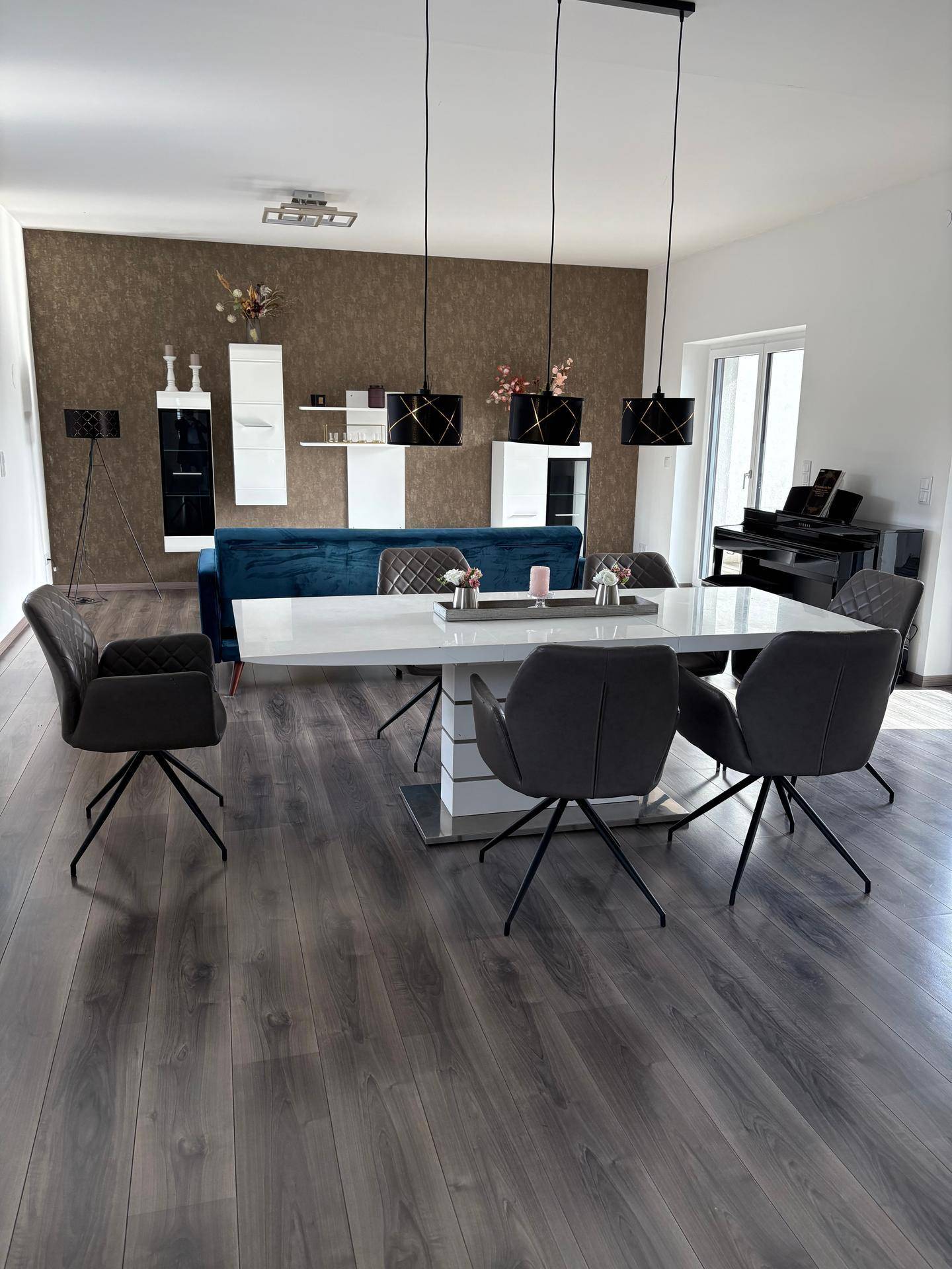 Moderner offener Wohn-Essbereich mit dunklem Holzboden, elegantem Esstisch und blauer Couch.