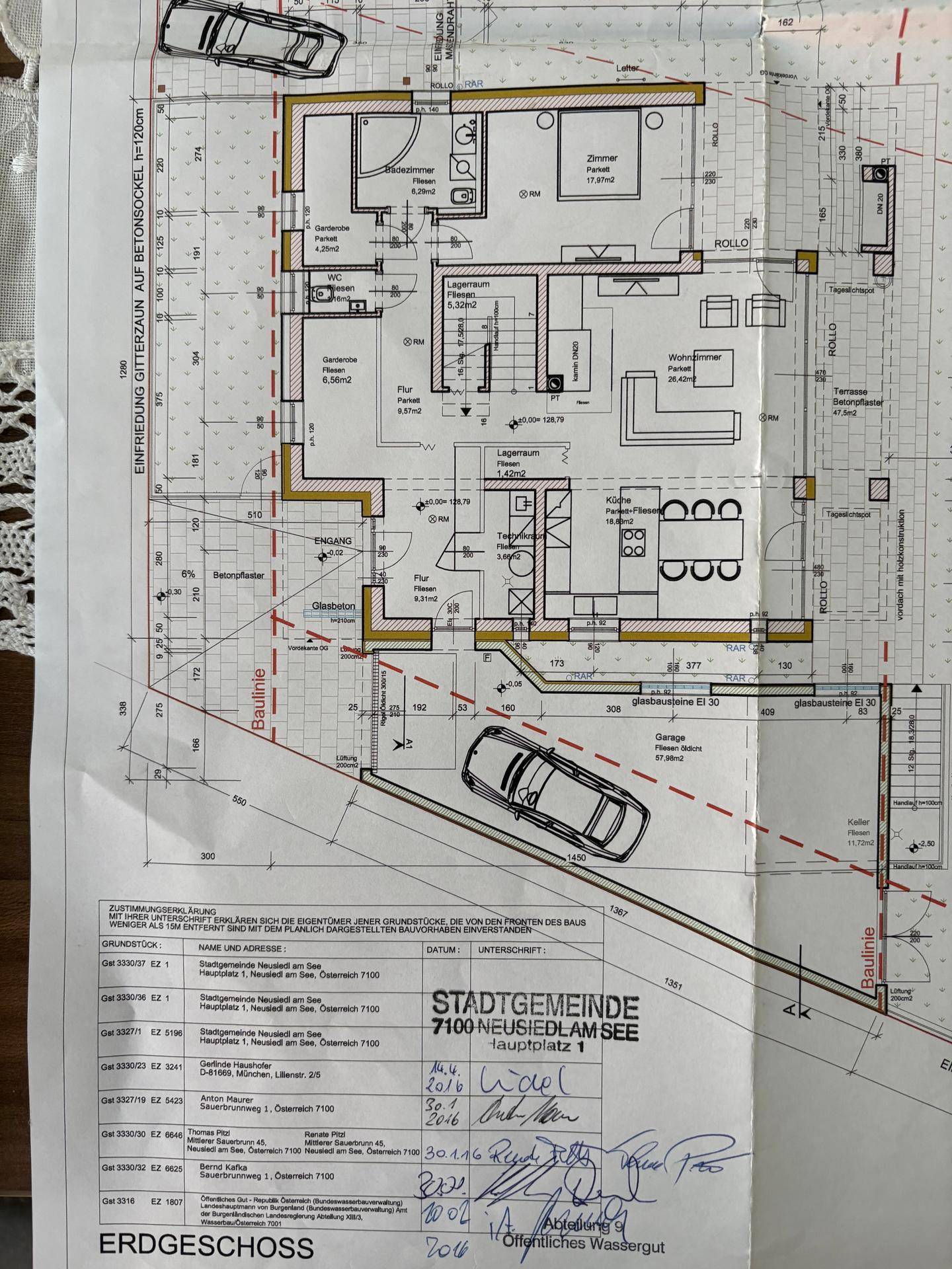 Grundriss des Erdgeschosses mit Wohnbereich, Küche und Garage, teilweise von einem Dokument überdeckt.