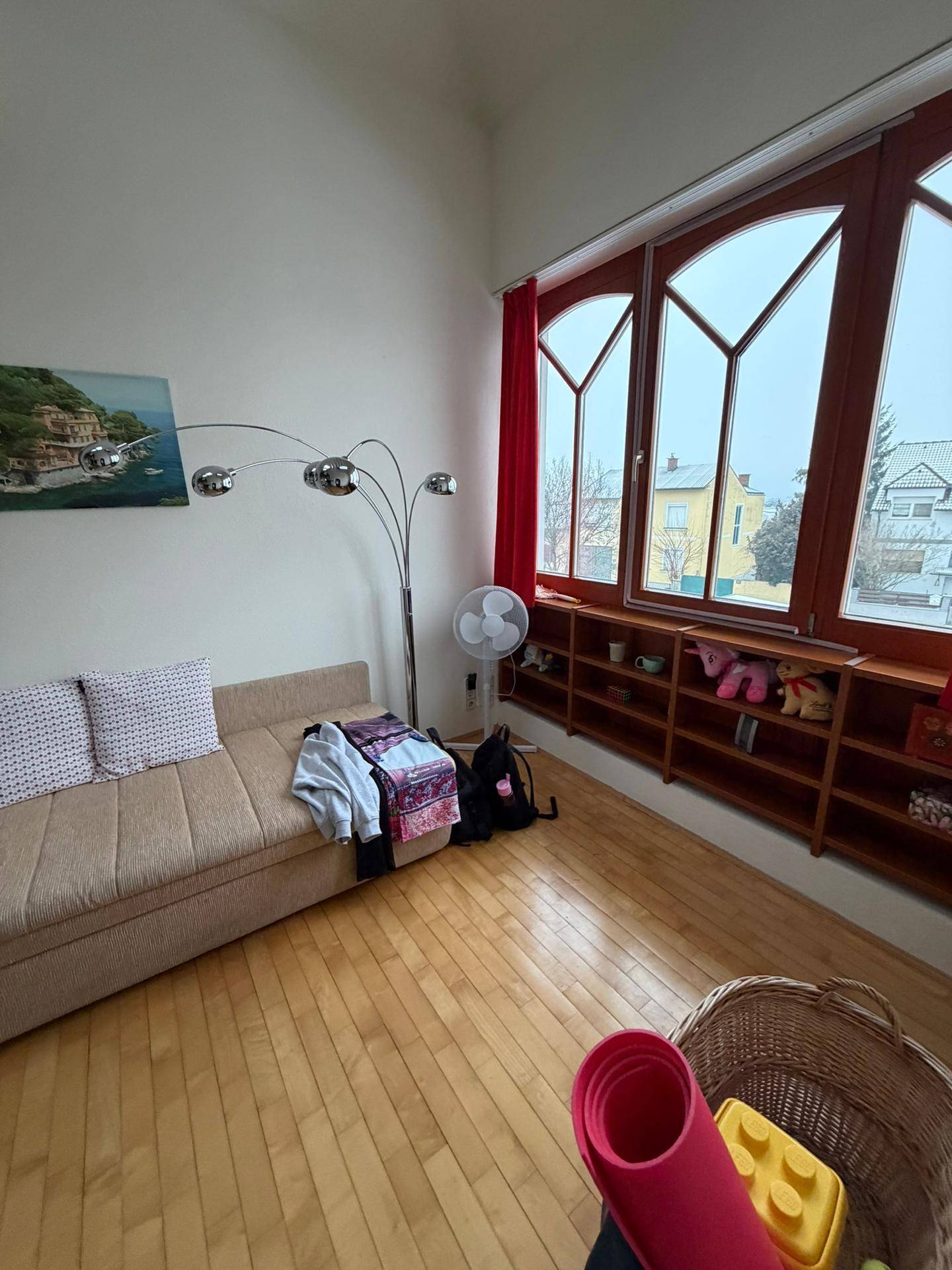 Gemütlicher Raum mit Holzboden, beigem Sofa und großen, bogenförmigen Fenstern.