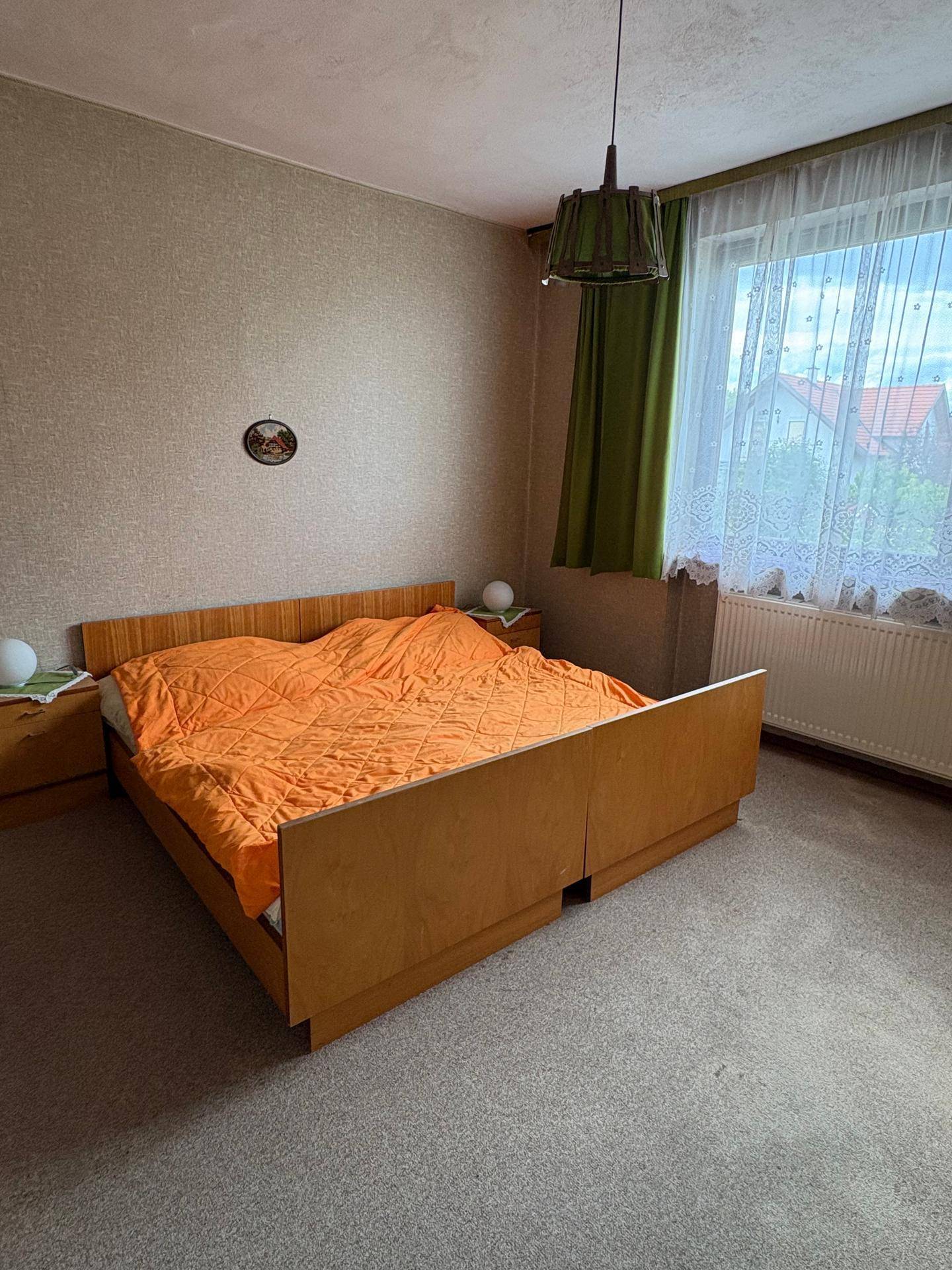 Schlafzimmer mit Teppichboden, Holzdecke und Fenster mit Blick ins Grüne.