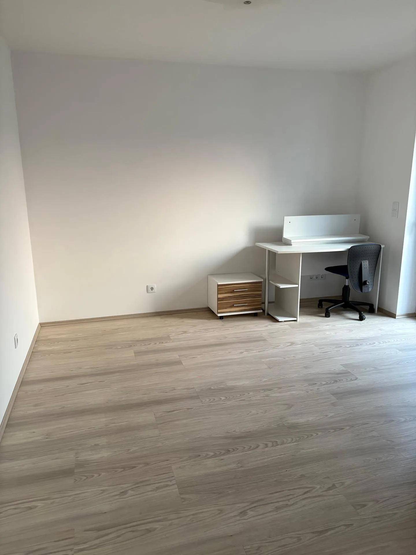 Helles Arbeitszimmer mit Laminatboden und einem einfachen Schreibtisch in minimalistischem Stil.