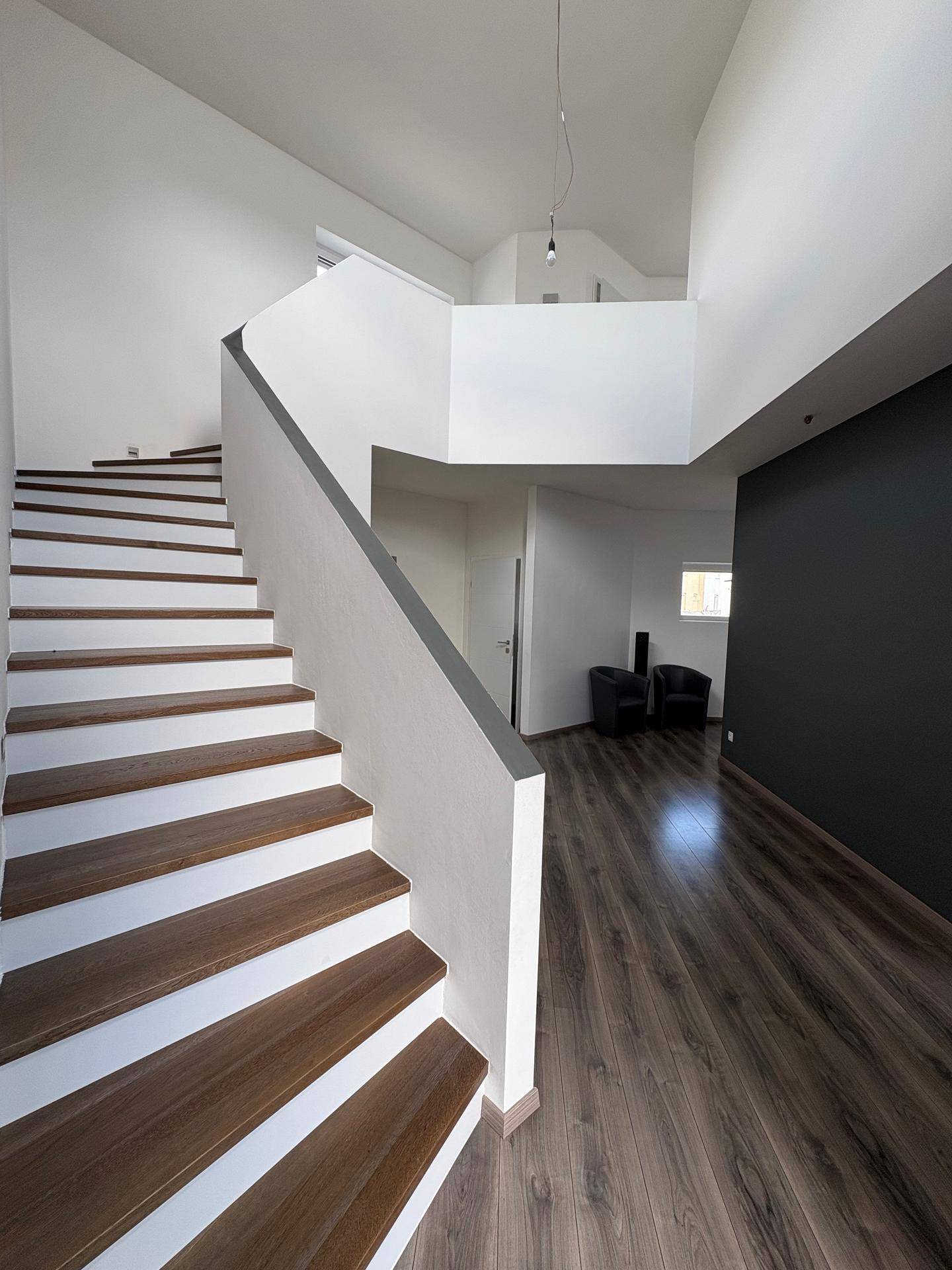 Heller Eingangsbereich mit moderner Holztreppe, hohen Decken und dunkler Akzentwand.