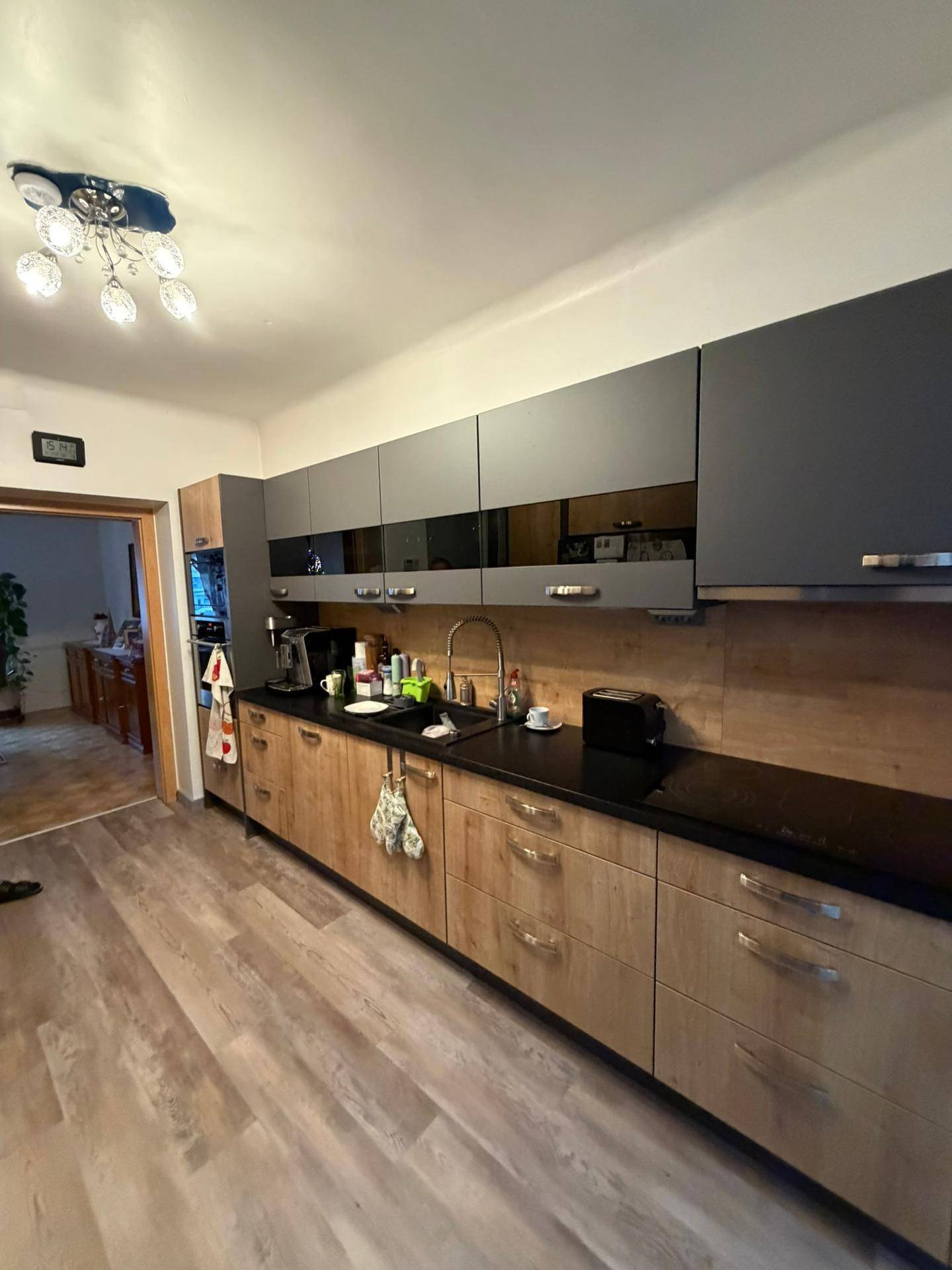 Moderne Küche mit grauen Oberschränken, Holzunterschränken und schwarzer Arbeitsplatte.