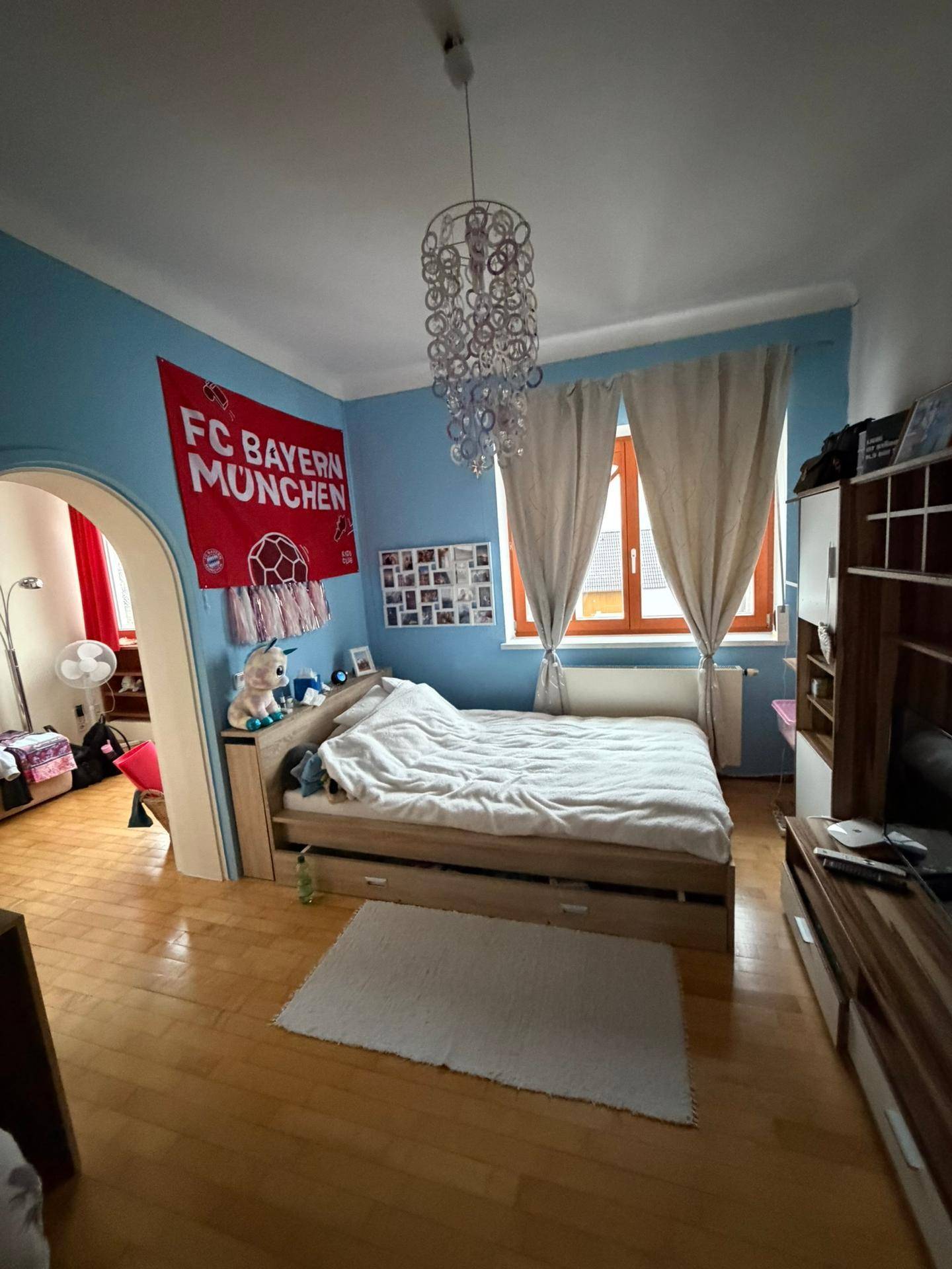 Helles Schlafzimmer mit Holzboden, blauen Wänden und einem großen Fenster mit Vorhängen.