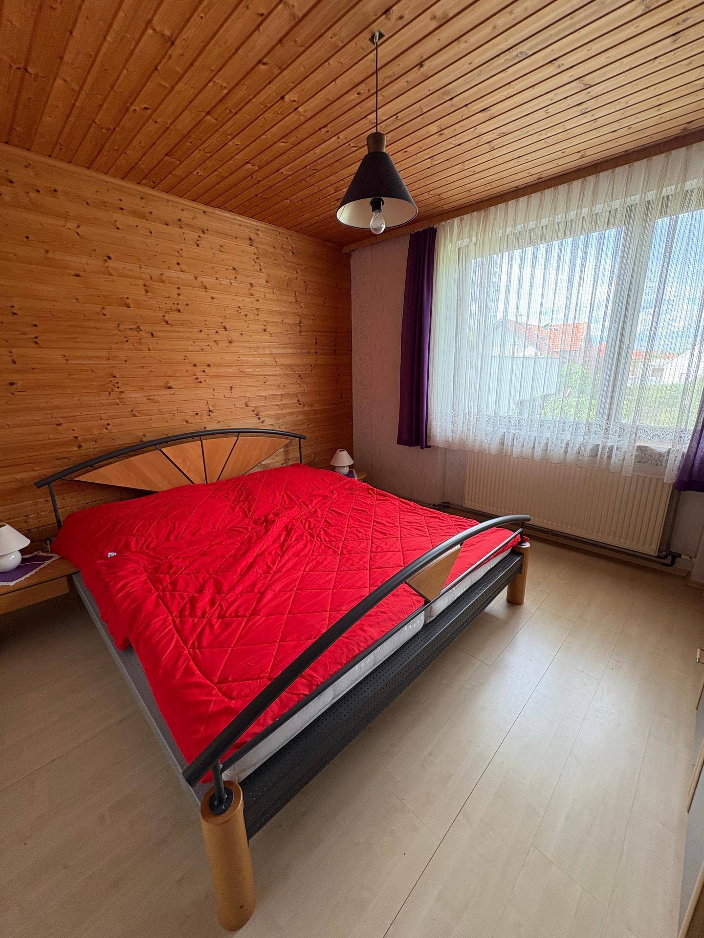 Gemütliches Schlafzimmer mit Holzvertäfelung, Parkettboden und großem Fenster.