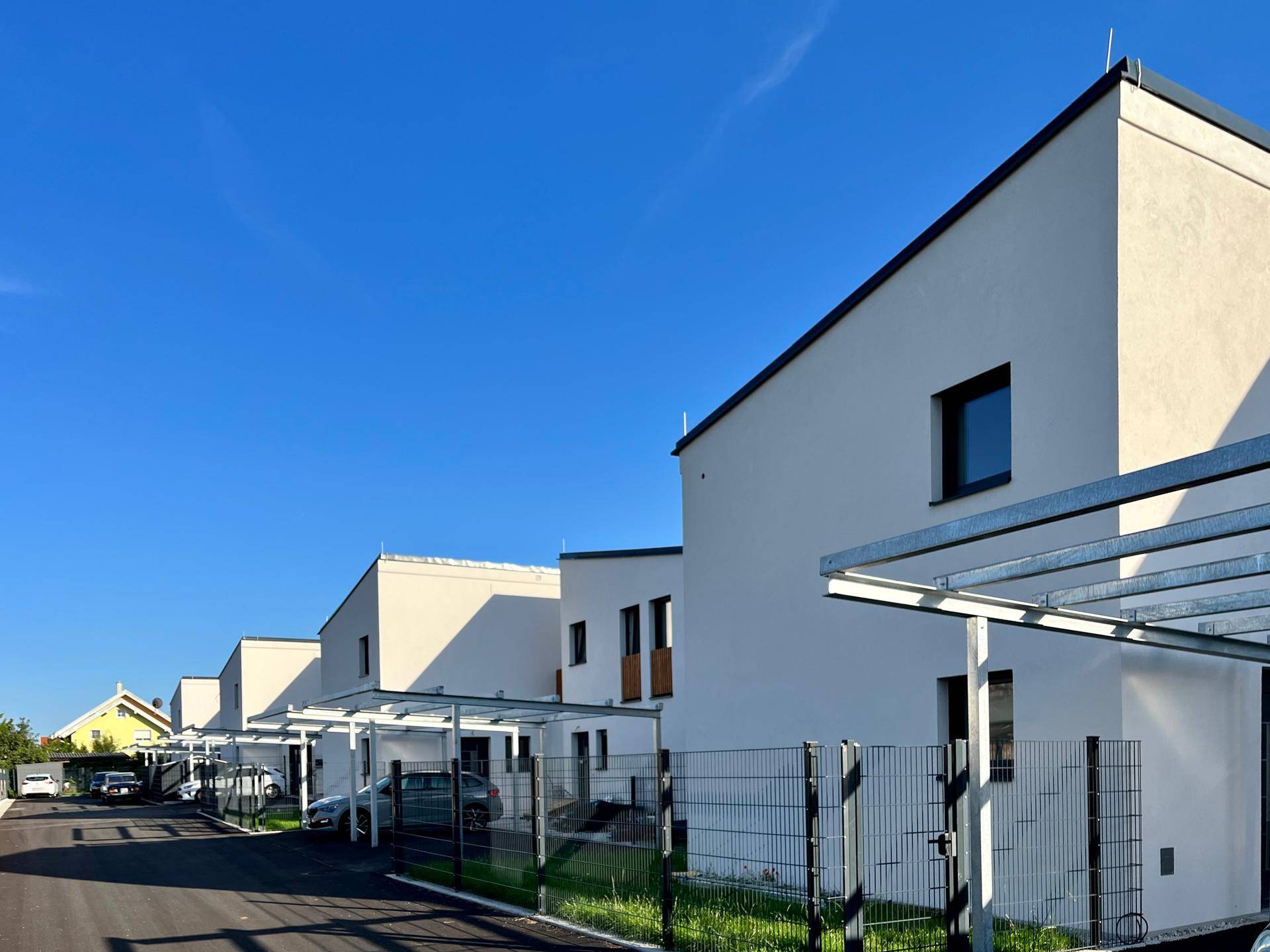 Reihe moderner Neubauten mit integrierten Carports unter strahlend blauem Himmel.