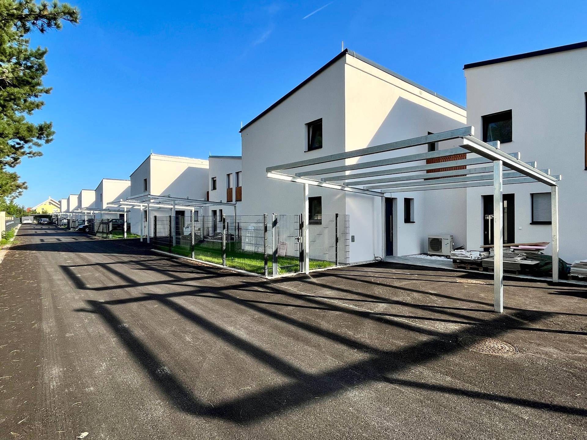 Reihe moderner Reihenhäuser mit Carports und Zufahrt unter klarem blauem Himmel.