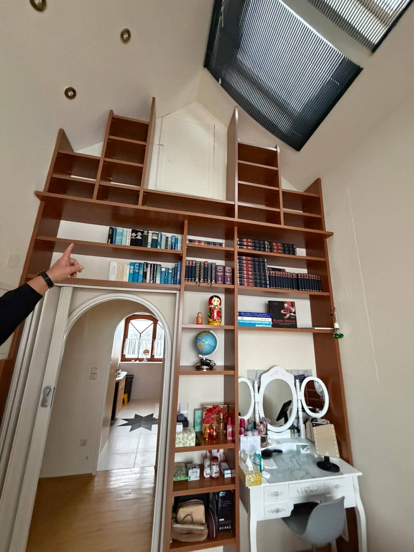 Raum mit sehr hohen Decken, großem Einbauregal, Schminktisch und Dachfenster.