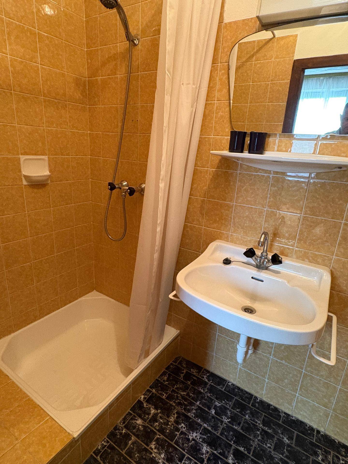Badezimmer mit gelben Fliesen, Dusche und Waschbecken in älterem Zustand.