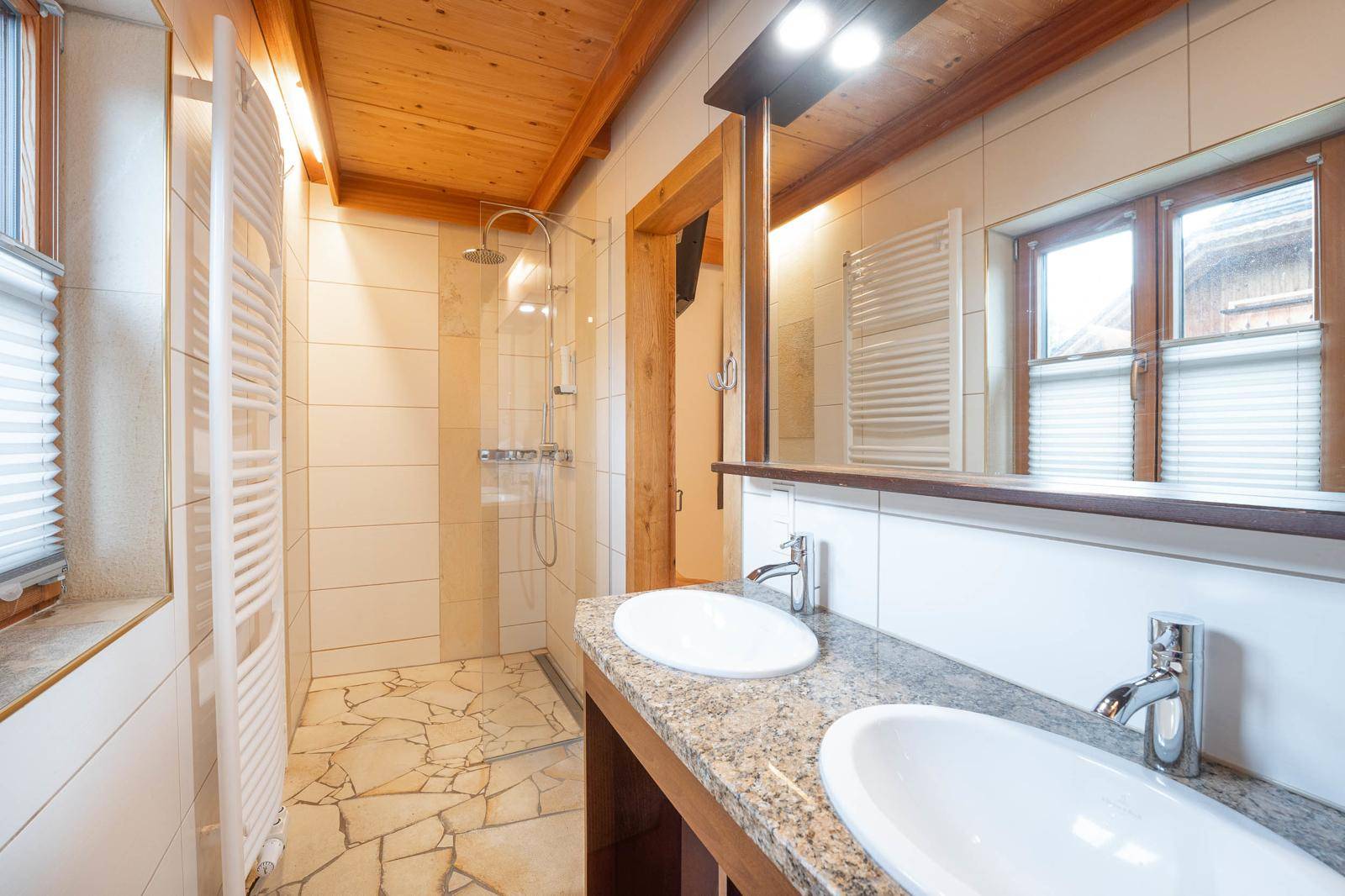 Modernes Badezimmer mit Doppelwaschbecken, begehbarer Dusche und Holzbalkendecke.
