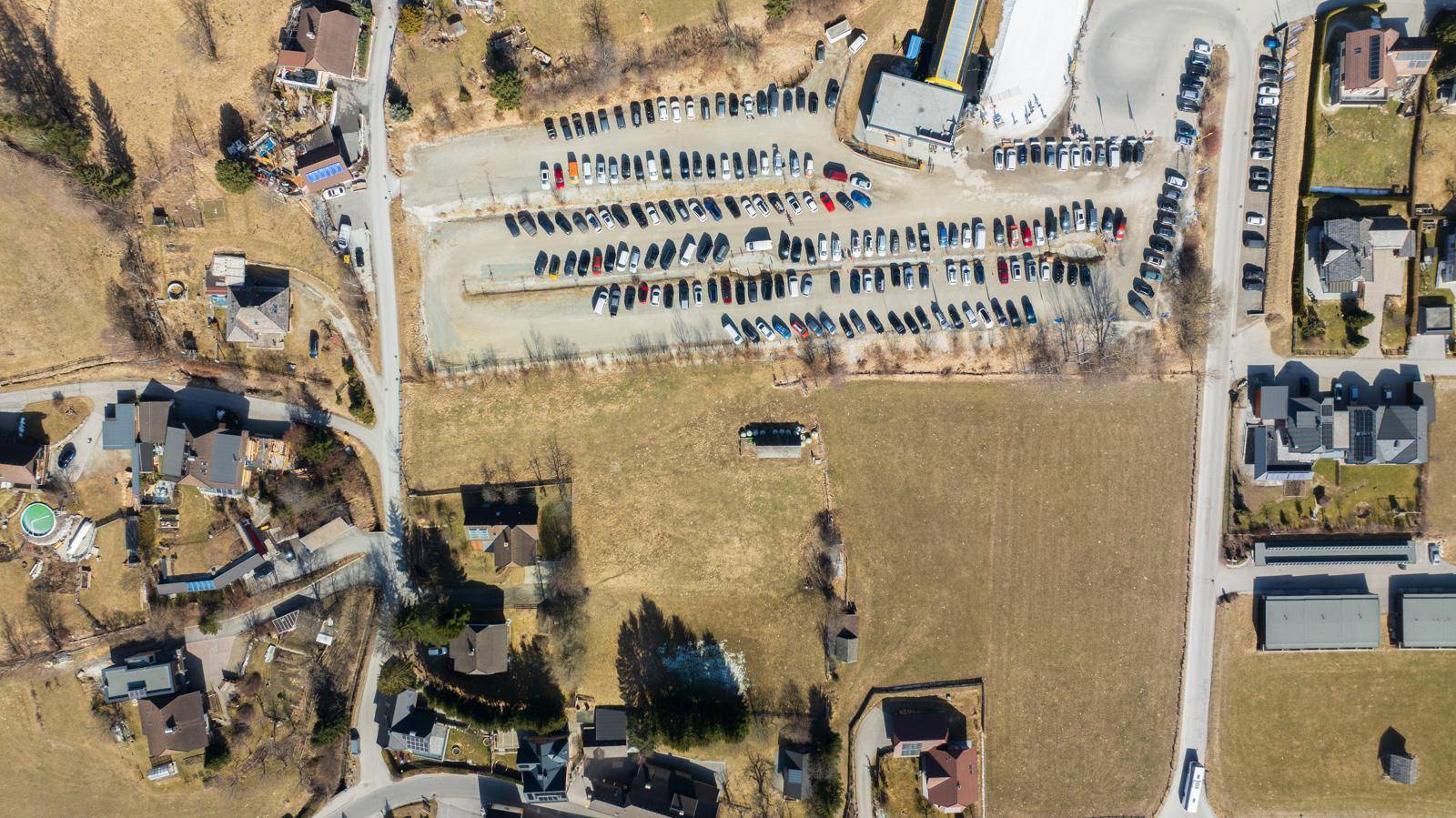 Detaillierte Luftaufnahme eines großen Parkplatzes umgeben von Feldern und Wohnhäusern in ländlicher Umgebung.