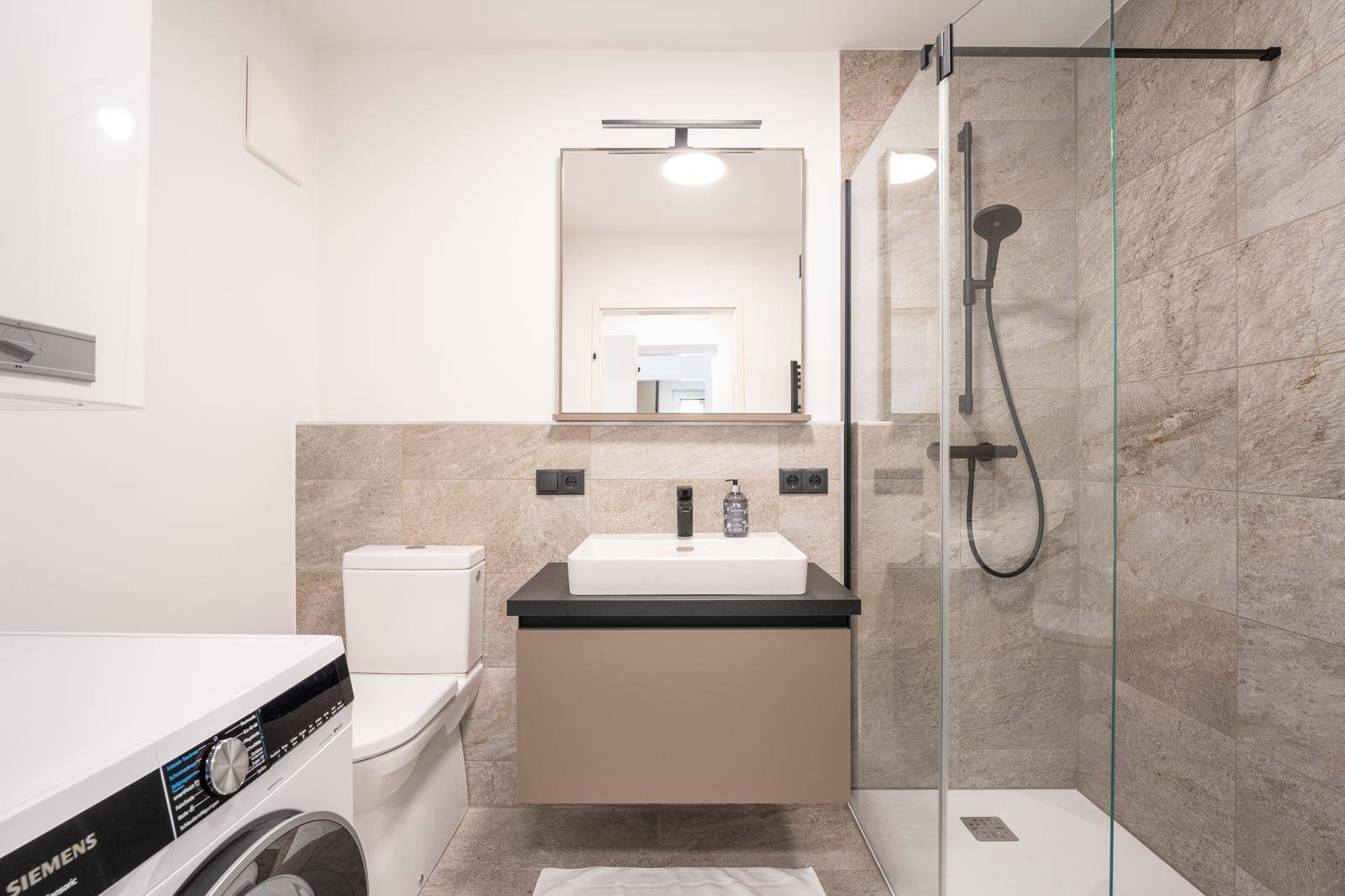 Modernes Badezimmer mit Dusche, Waschmaschine und eleganten Fliesen.