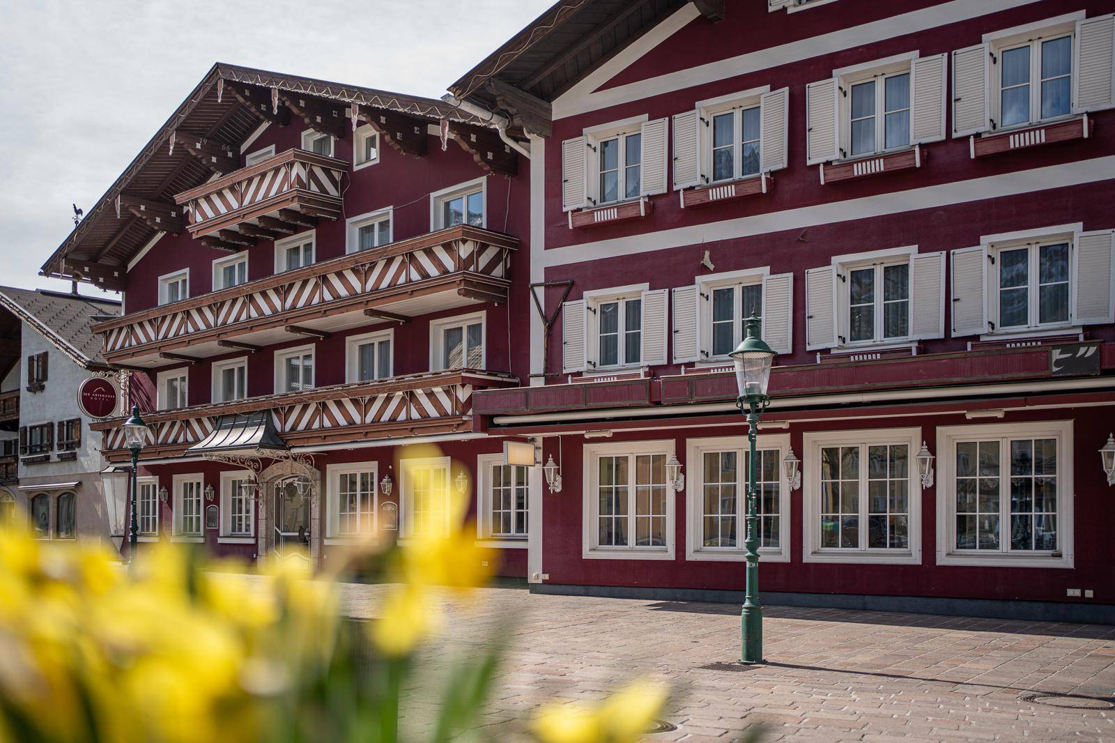 Rotes Gebäude im traditionellen Stil mit weißen Fensterläden und Holzbalkonen, umgeben von Frühlingsblumen.