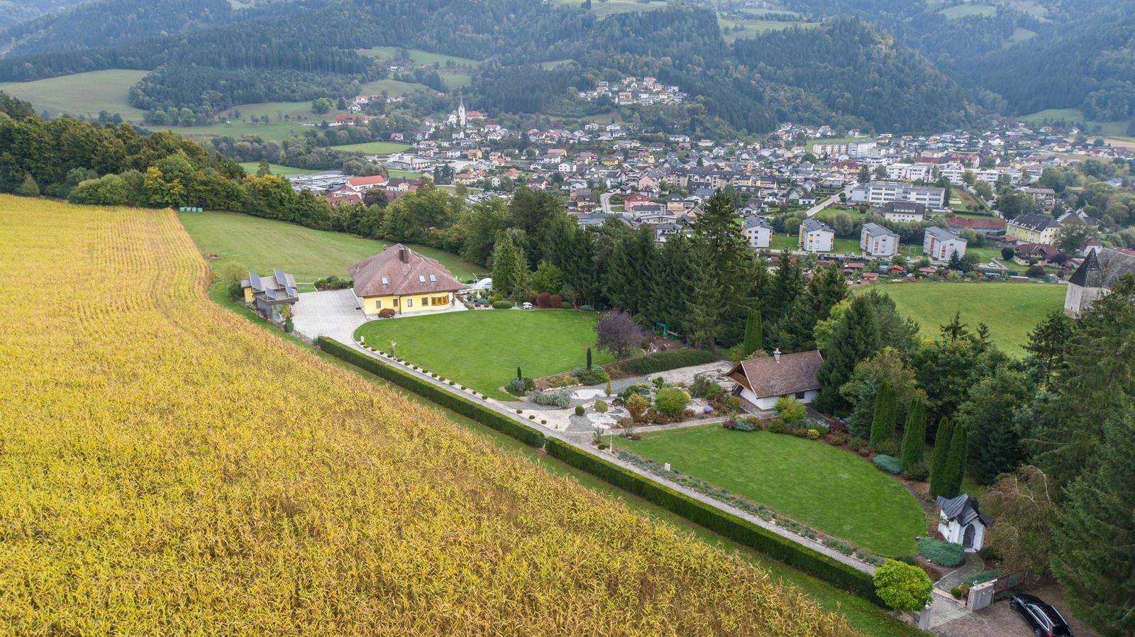 Weitläufige Luftaufnahme des Anwesens mit großem Garten und Blick auf eine nahegelegene Ortschaft.