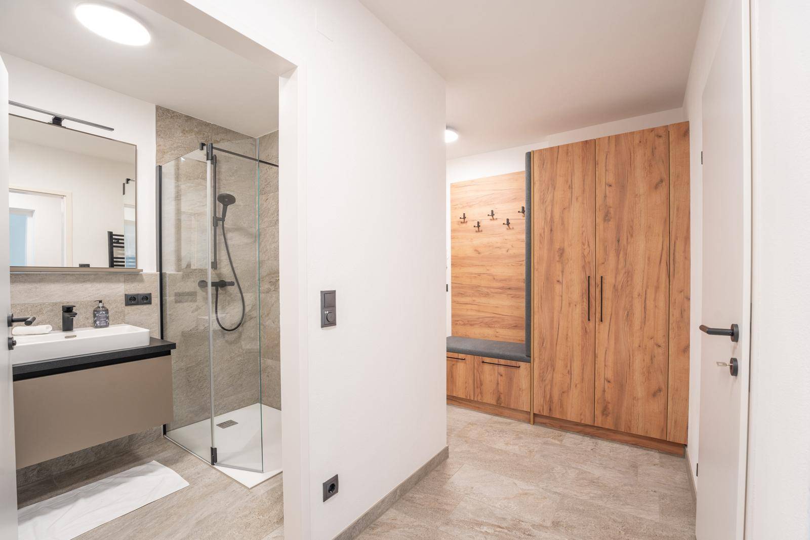 Eingangsbereich mit integriertem Garderobenschrank und Blick ins moderne Badezimmer.