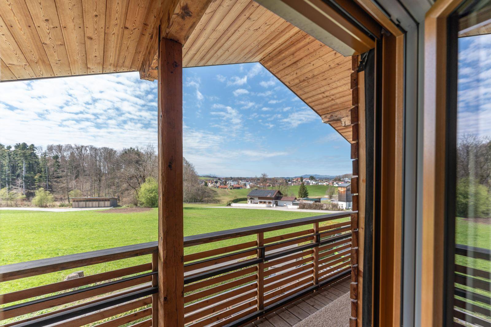 Geräumiger Holzbalkon mit weitem Blick über grüne Wiesen und die umliegende Natur, ideal zum Entspannen.