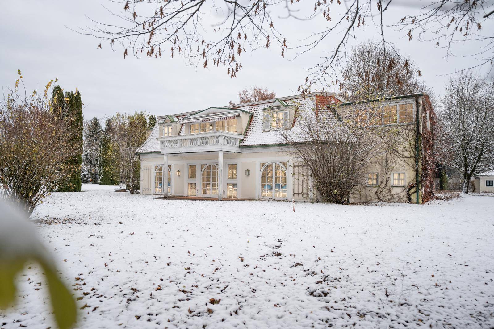 Weitläufiger verschneiter Garten mit eleganter Villa und umliegenden Bäumen.