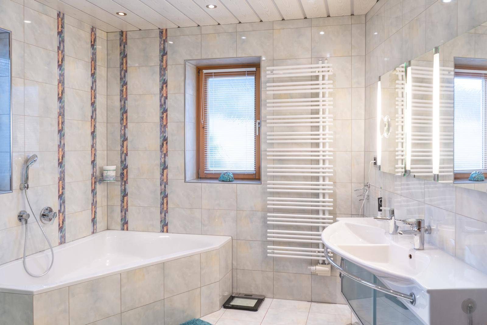 Modern gefliestes Badezimmer mit Eckbadewanne, Einzelwaschbecken und beheiztem Handtuchhalter.