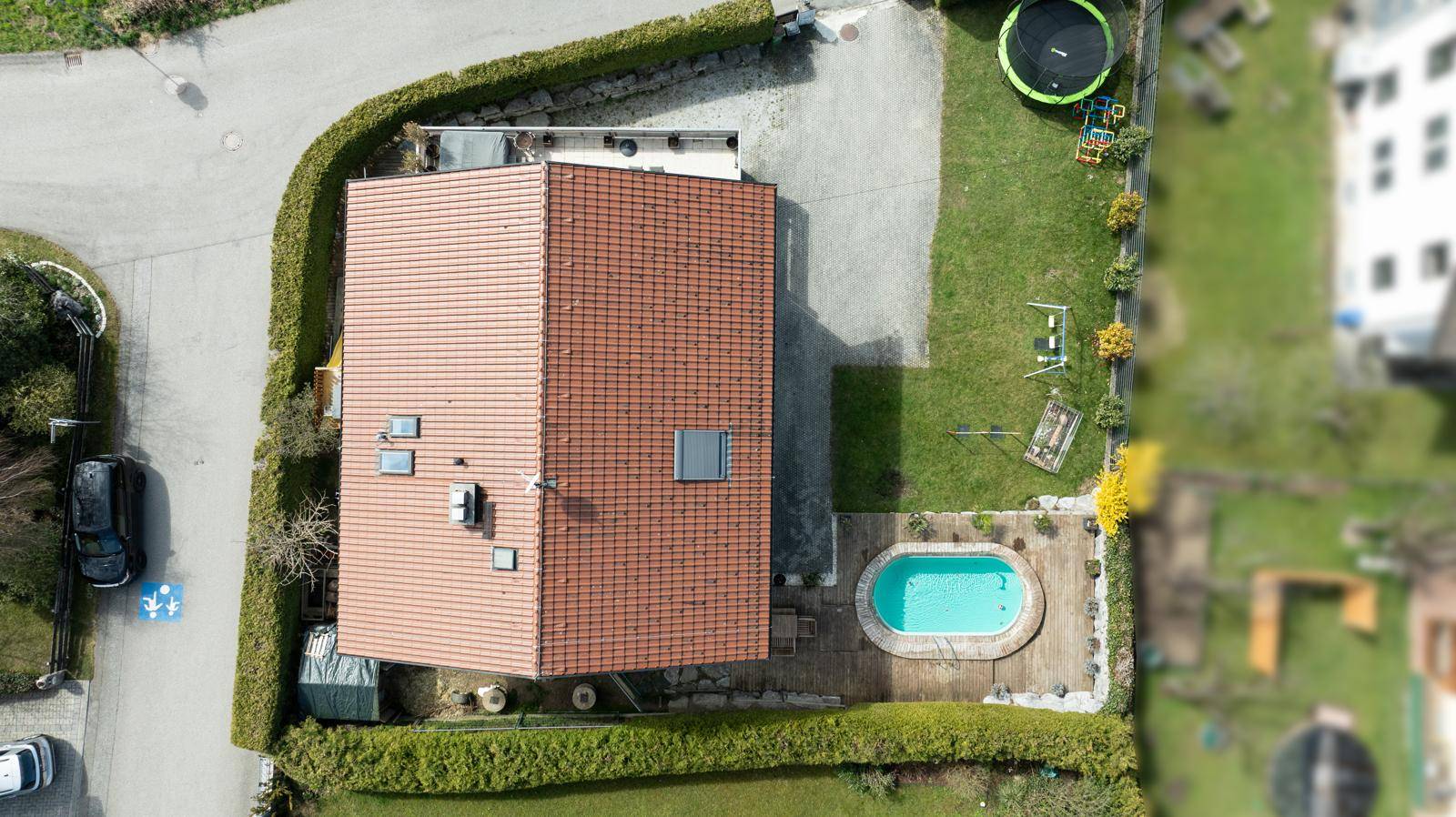 Draufsicht auf das Grundstück mit Haus, Garten, Pool und Trampolin, umgeben von Hecken und Wegen.