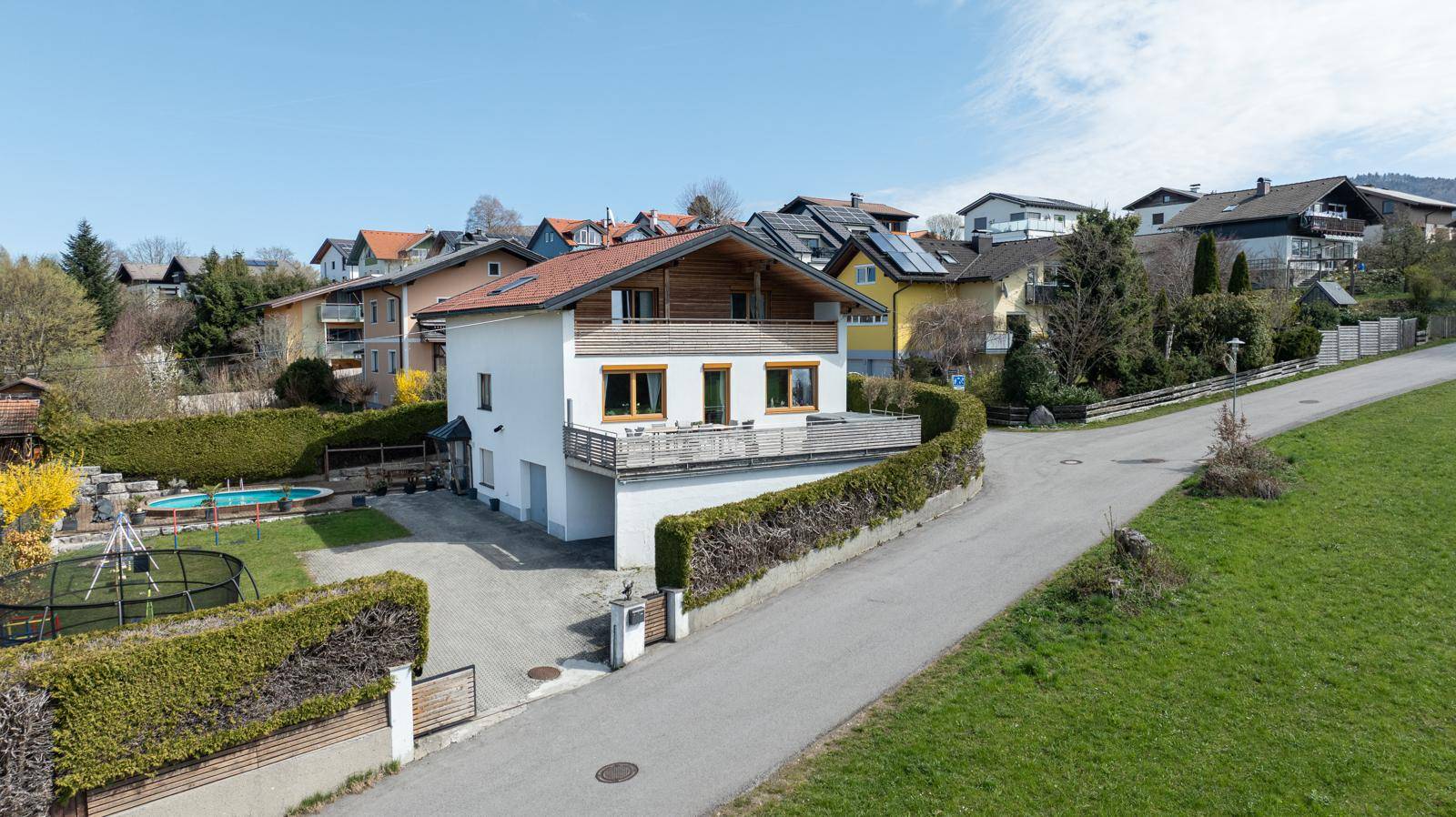 Einfamilienhaus mit gepflegtem Garten, Pool und Spielbereich, umgeben von einer Hecke und ländlicher Idylle.