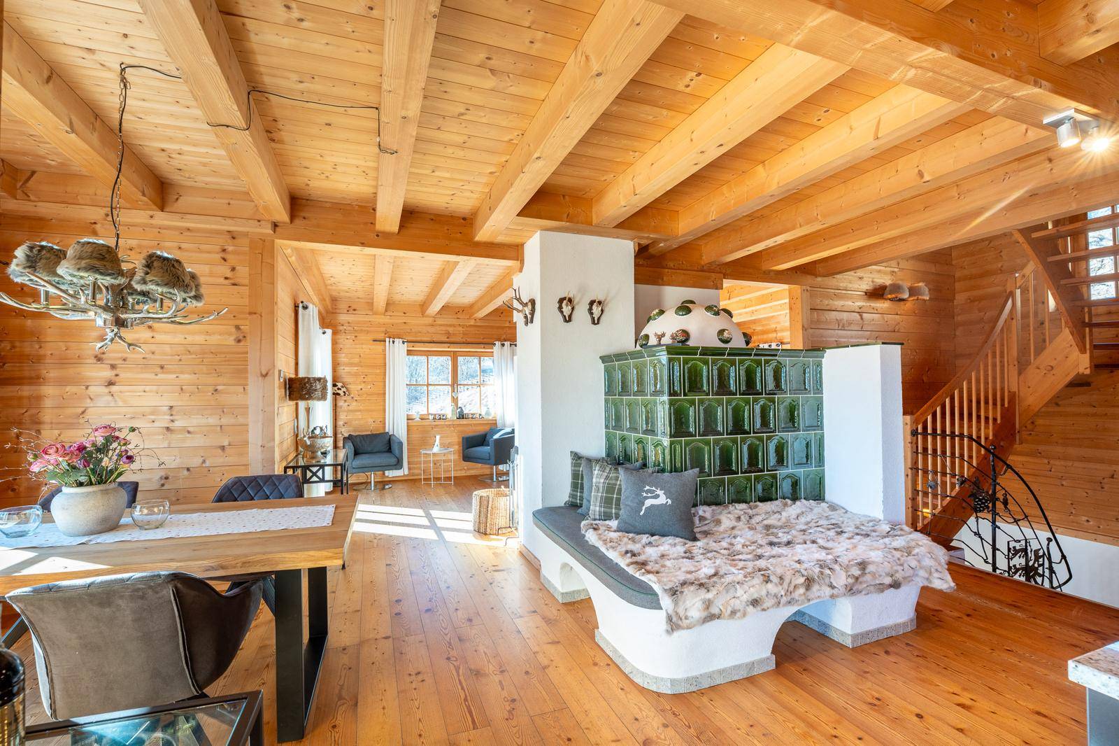 Gemütlicher Wohn- und Essbereich im alpinen Stil mit Kachelofen, Holzbalkendecke und Holzboden.