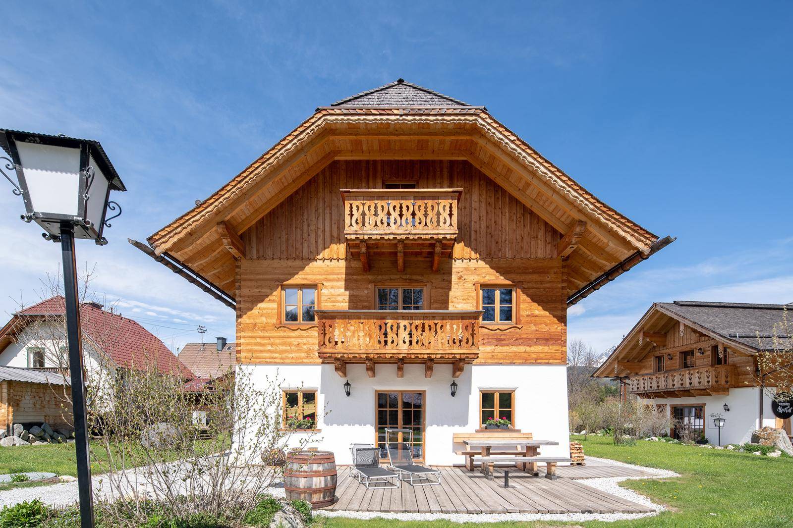 Traditionelles Holzhaus im Chalet-Stil mit Balkonen und einer möblierten Terrasse im Grünen.