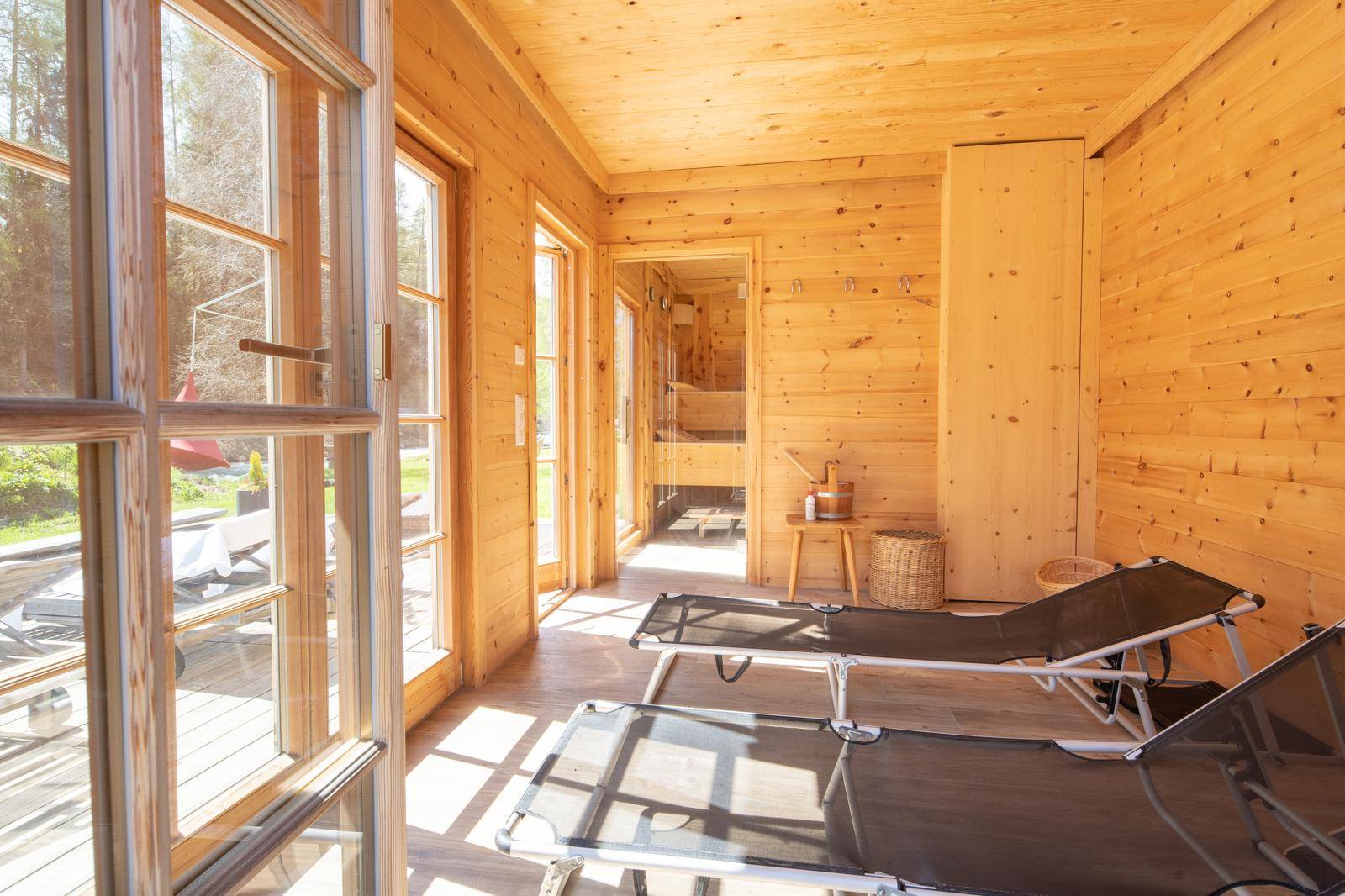 Entspannungsbereich mit Liegestühlen und großen Fenstern, angrenzend an die Sauna.