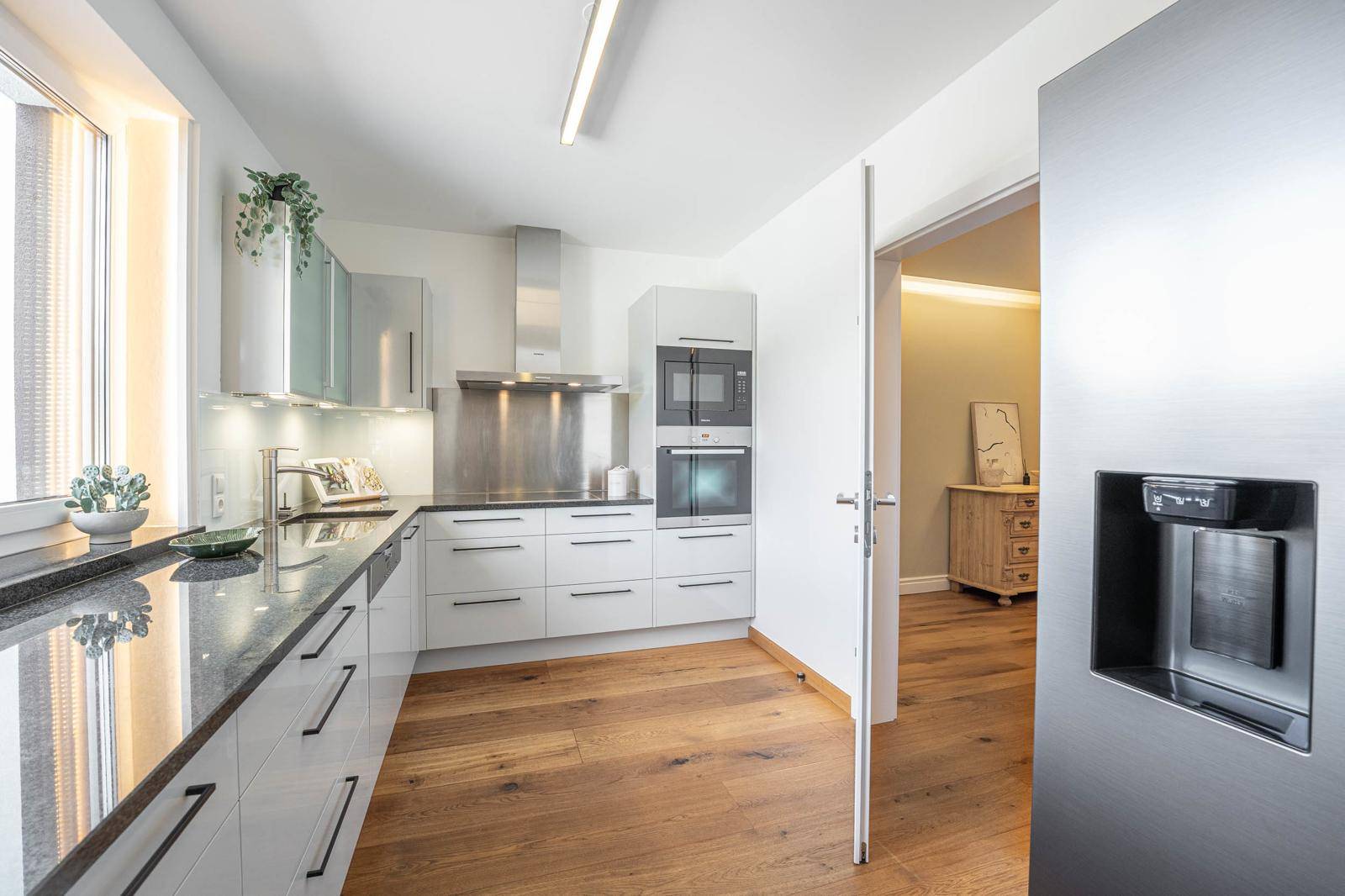 Moderne Küche mit weißen Hochglanzfronten, Granitarbeitsplatte und integrierten Geräten.