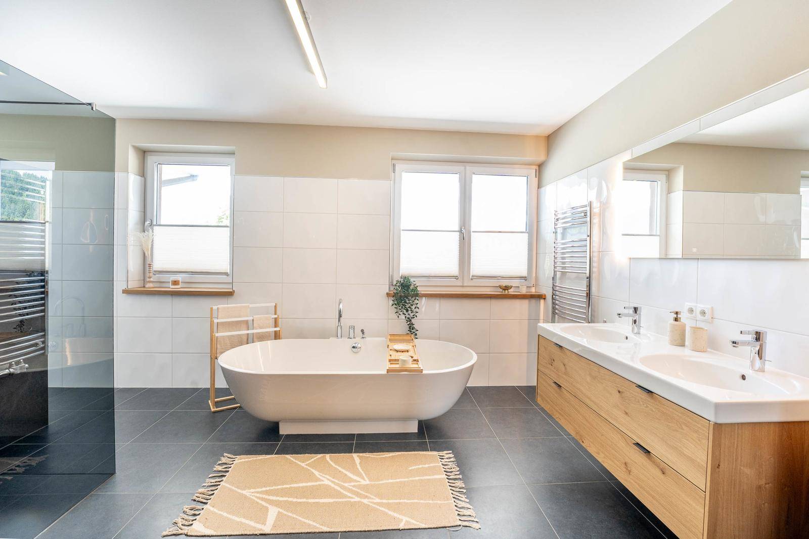 Modernes Badezimmer mit freistehender Badewanne, Doppelwaschbecken und zwei Fenstern.