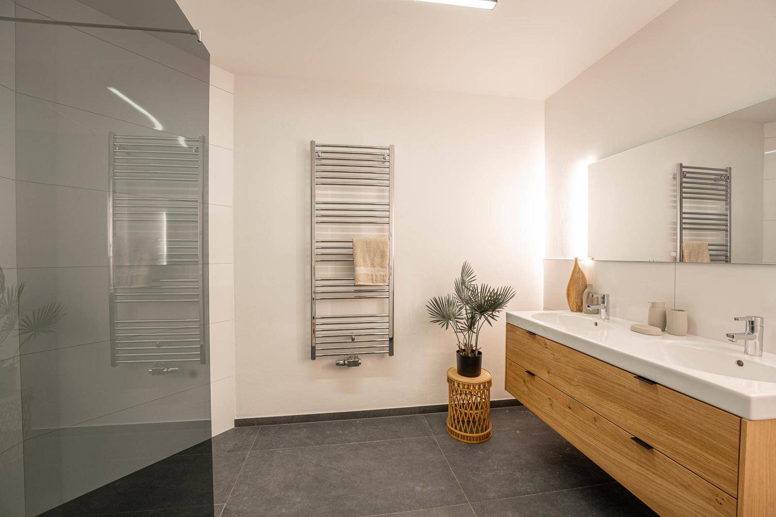 Modernes Badezimmer mit Doppelwaschbecken, großer Dusche und beheiztem Handtuchhalter.