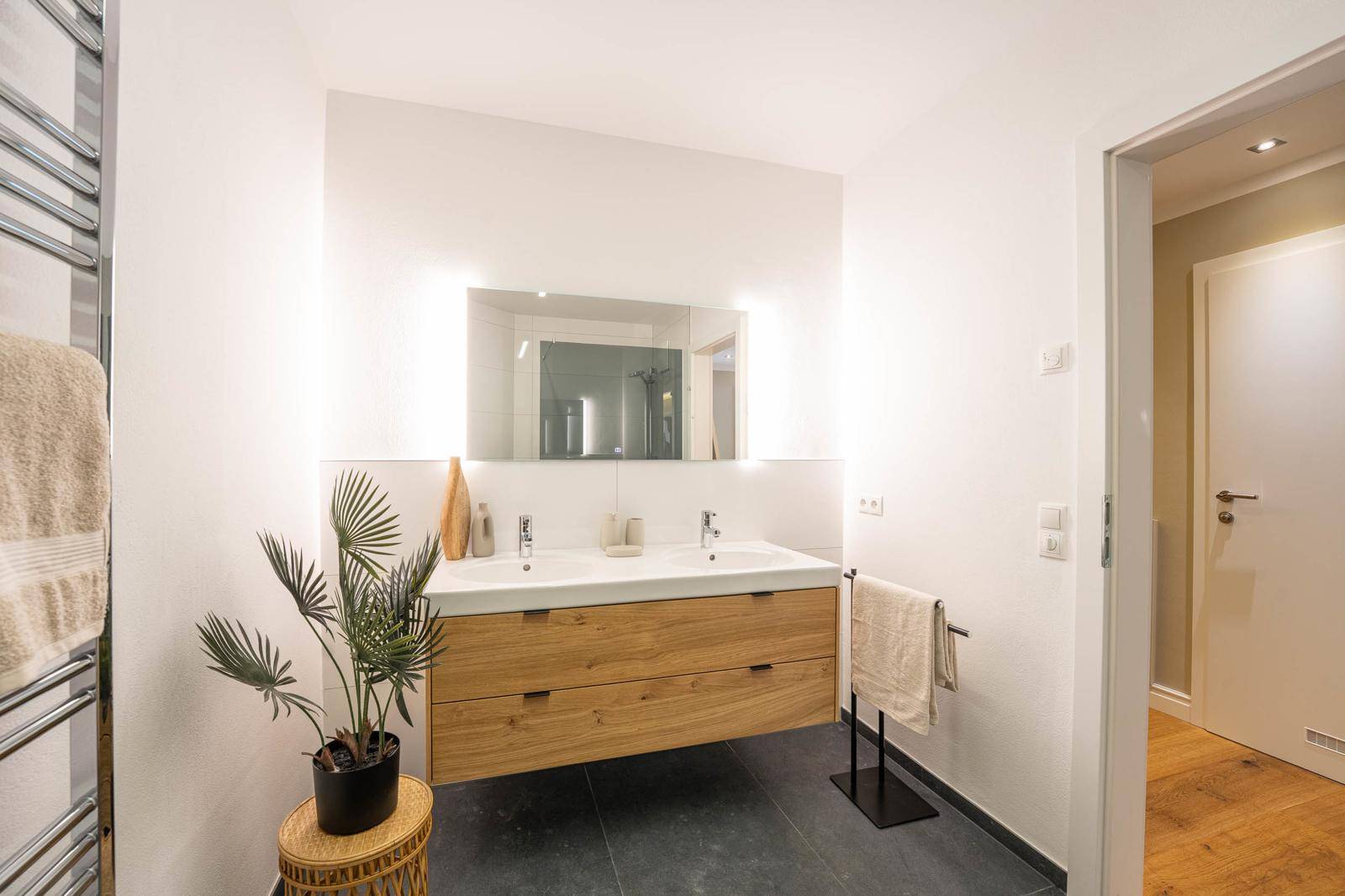 Helles Badezimmer mit Doppelwaschbecken, großem Spiegel und indirekter Beleuchtung.