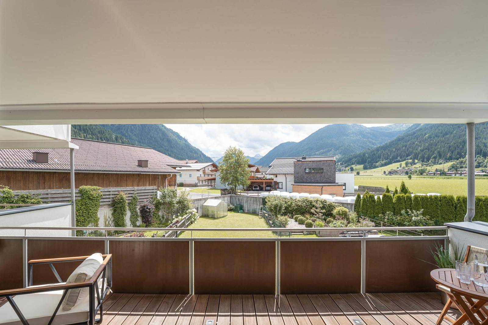 Weitläufiger Blick von einem Balkon über ein grünes Tal mit Häusern und majestätischen Bergen im Hintergrund.