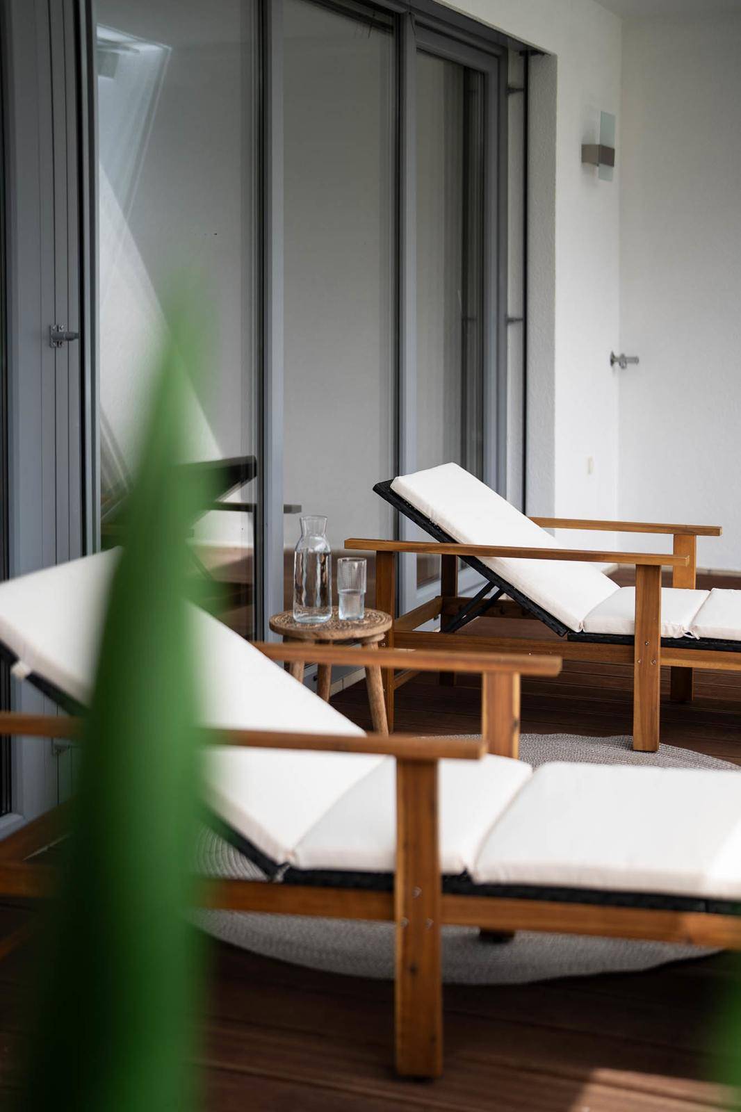 Detailansicht von Liegestühlen und einem kleinen Tisch auf einem sonnigen Balkon mit Holzdeck.