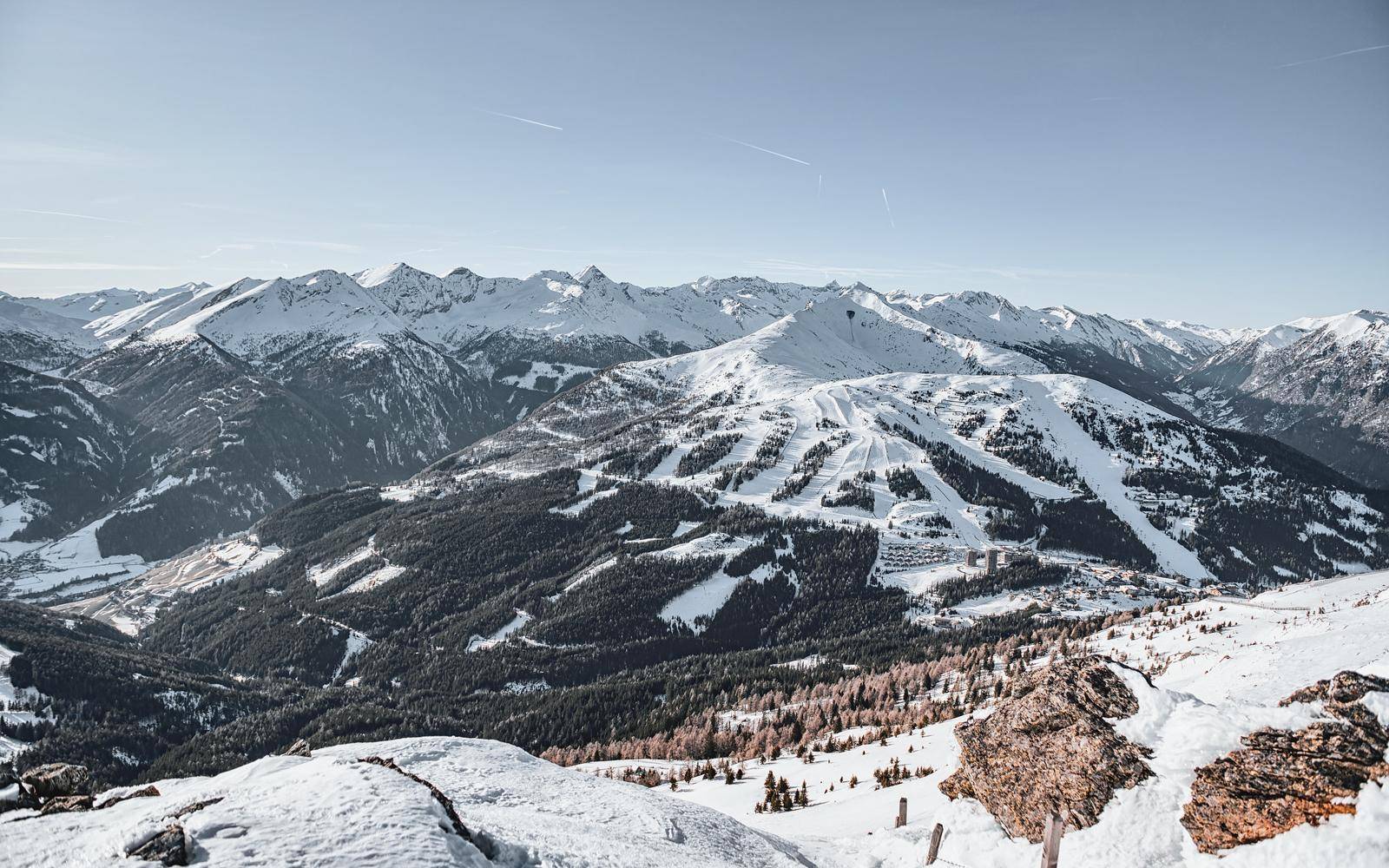 Eine weite Panoramaansicht einer schneebedeckten Berglandschaft mit Skipisten unter klarem Himmel.